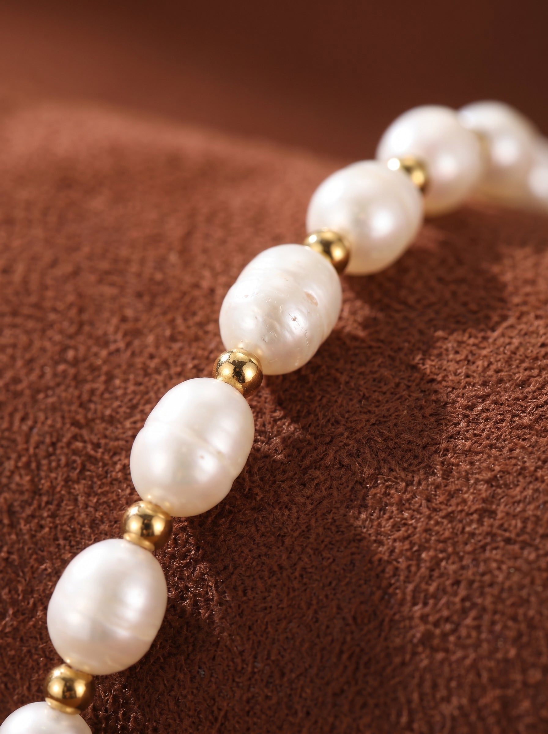 Close-up of a white freshwater pearl beaded bracelet with gold spacers on a brown textured surface. @pearl