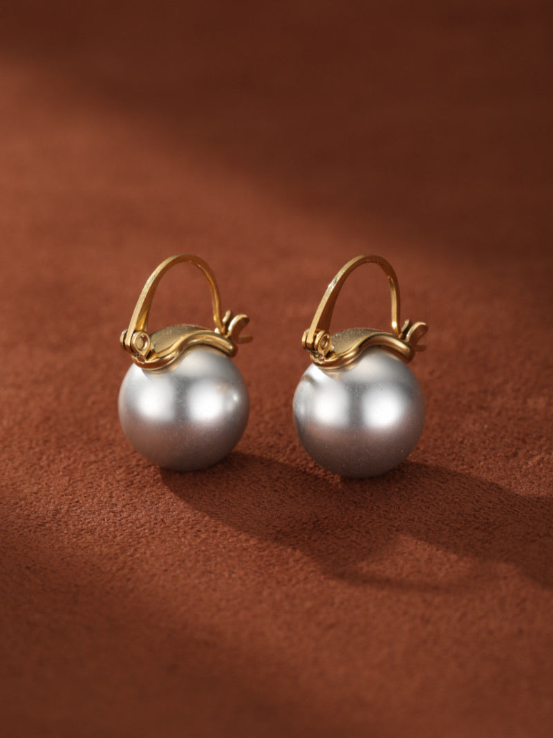 Gold hoop drop earrings featuring large, round, lustrous white freshwater pearls against a warm brown background.
