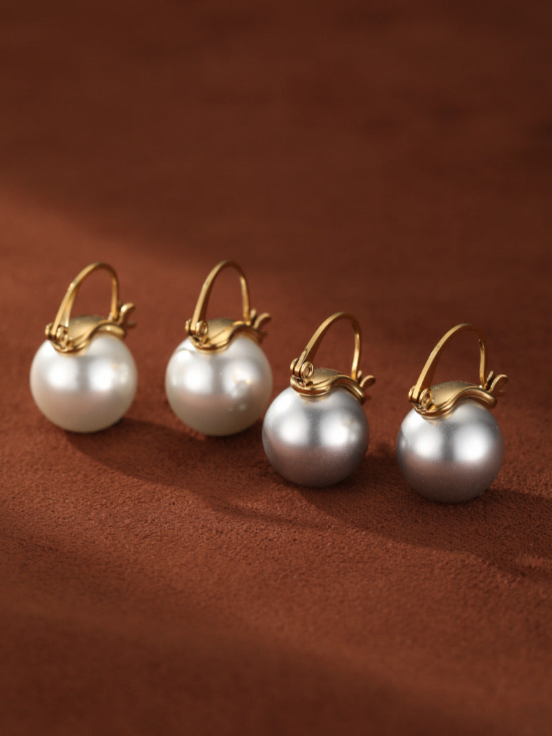 A pair of gold-toned hoop drop earrings featuring large, round white freshwater pearls against a textured brown background.