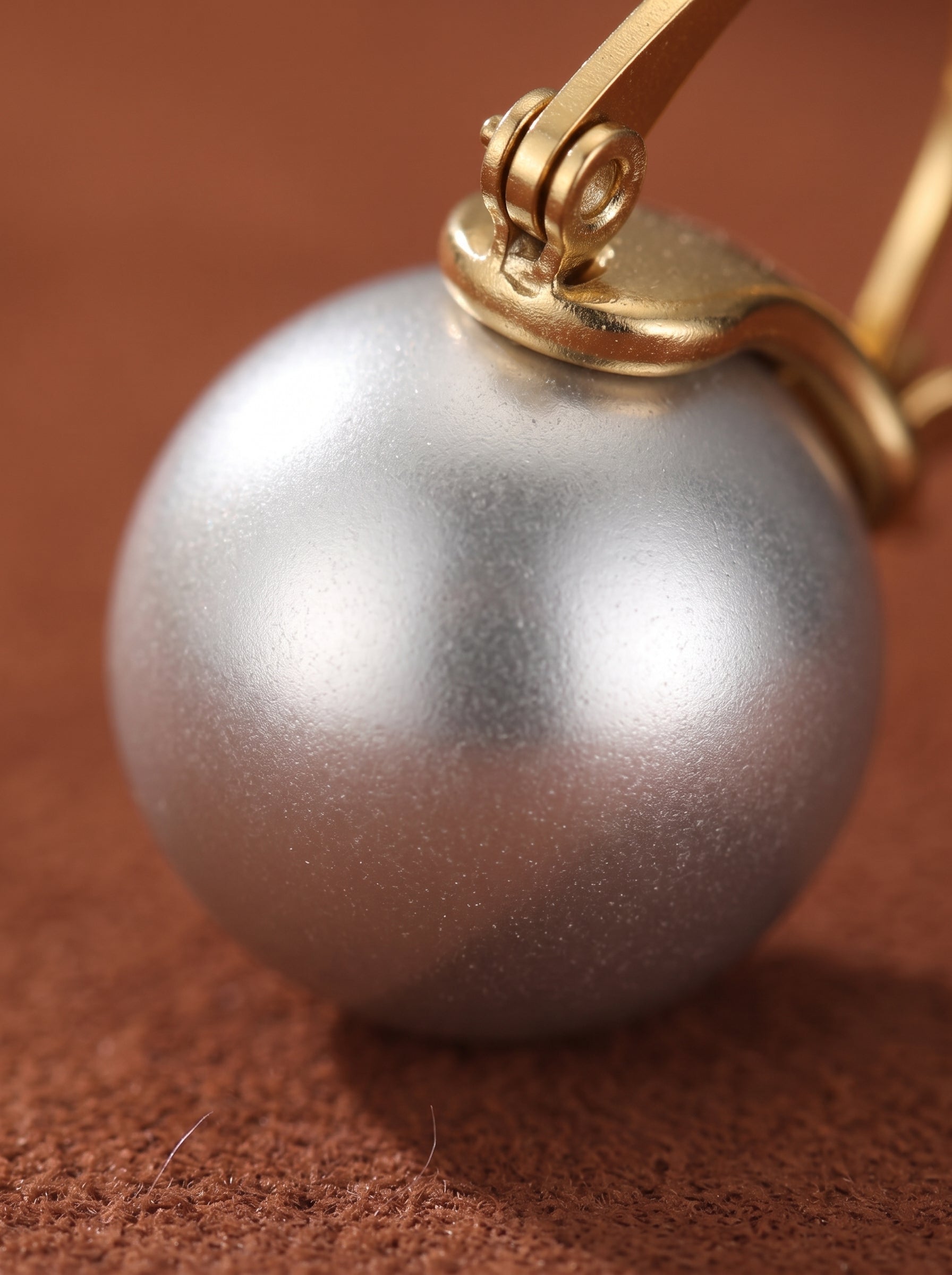 Close-up of a single, large, round, matte silver freshwater pearl suspended from a gold-toned hoop earring. @pearl