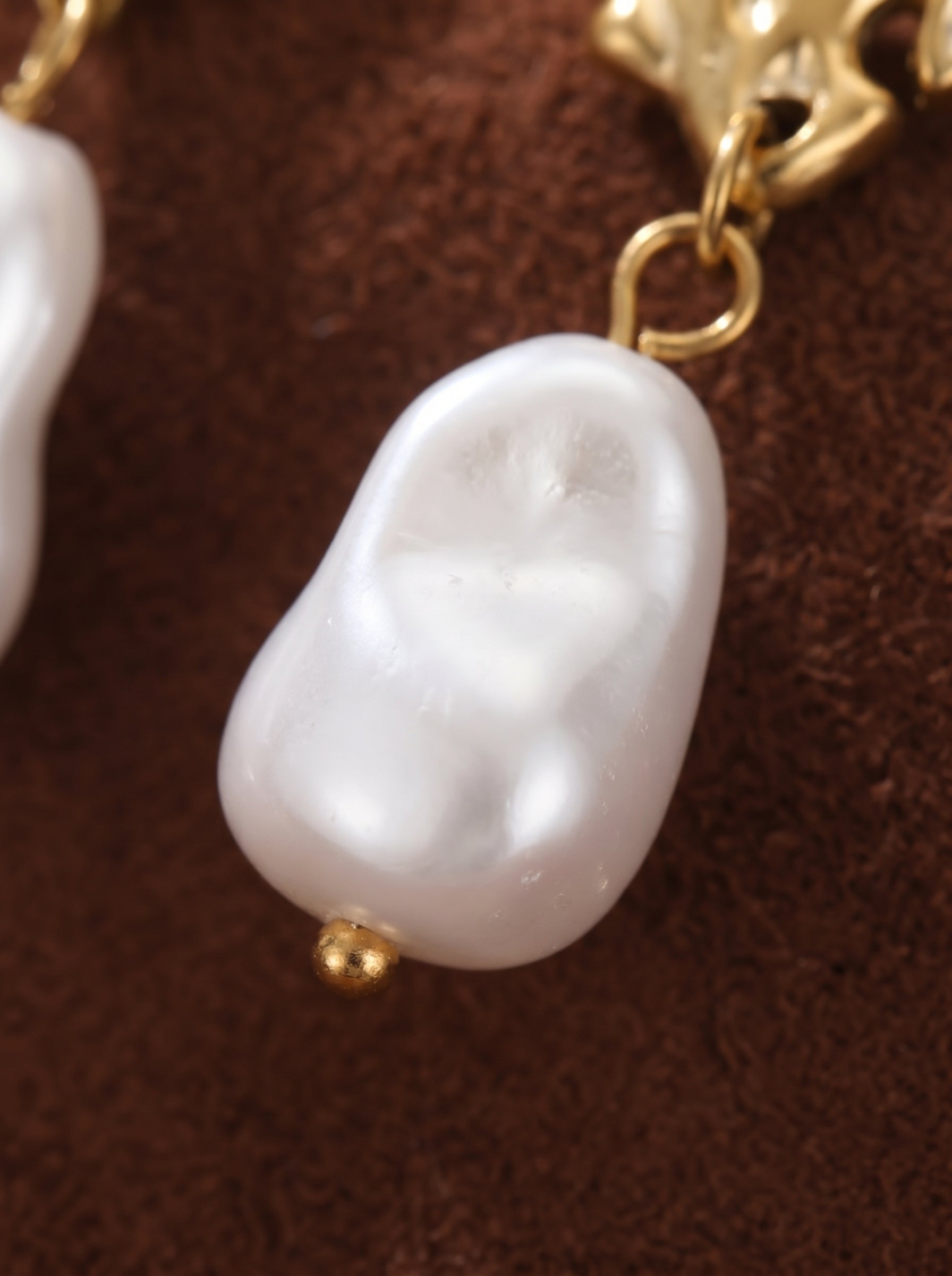 Close-up of Lumin Flame Drop Earrings showcasing a lustrous, organically shaped white freshwater pearl accented with a small gold bead, suspended from a textured gold flame-shaped hook. @pearl