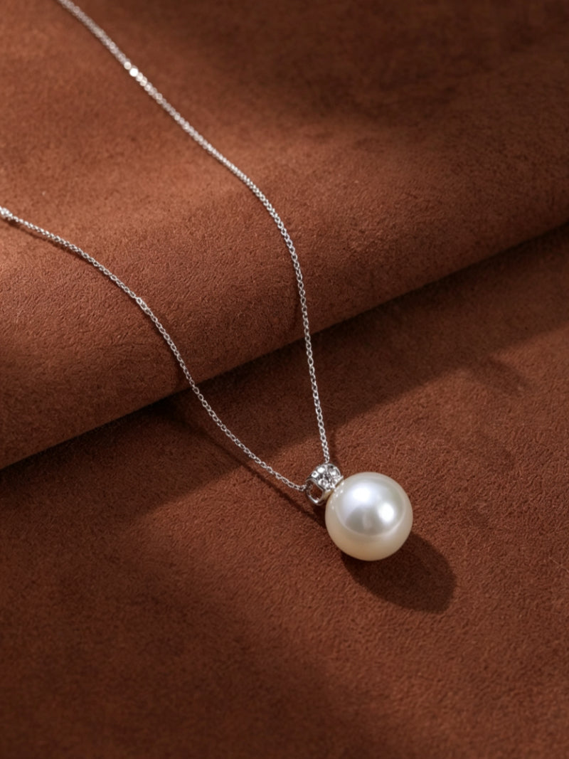 Lumin South Sea pearl chain drop necklace with a single, luminous pearl and a sparkling cubic zirconia accent, set against a rich brown textured background.