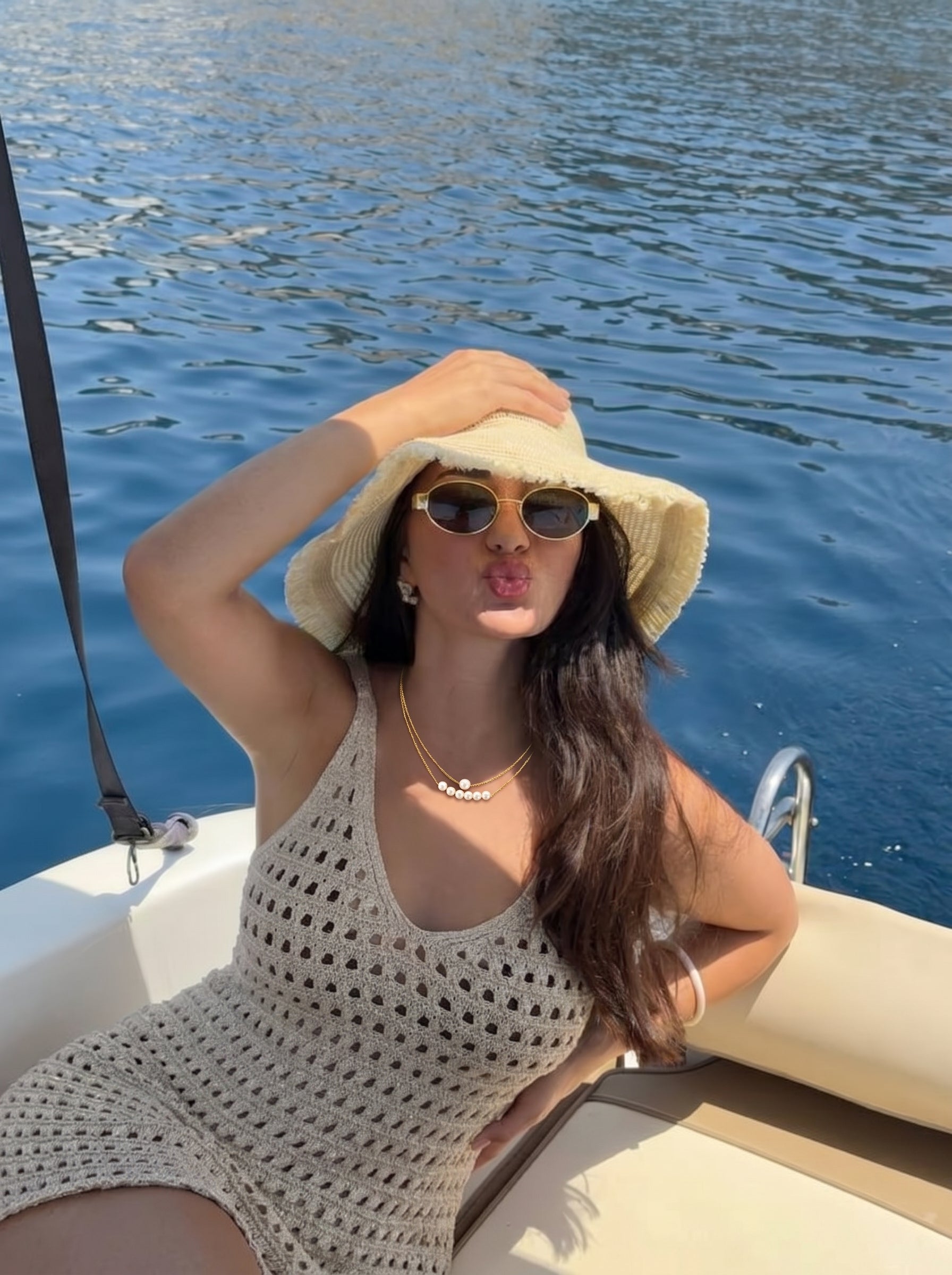 A woman wearing the Lumina imitation pearl layered chain necklace, a straw hat, and sunglasses, posing on a boat with blue water in the background. #lifestyle