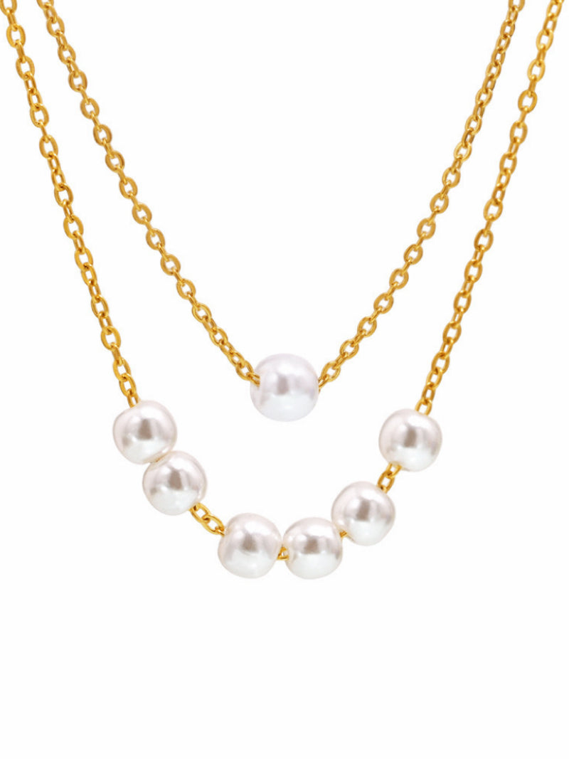 A delicate gold layered necklace featuring a strand of round white imitation pearls arranged in a subtle curve on the lower chain and a single pearl on the upper chain, against a white background.