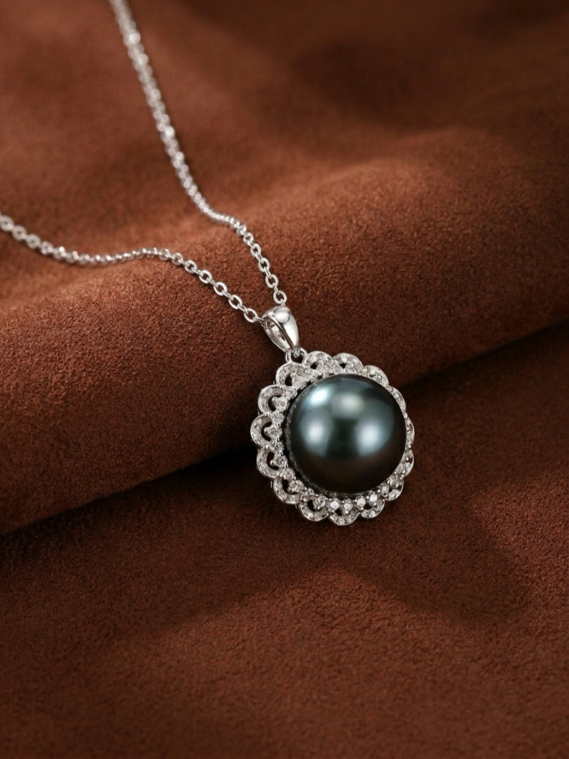 A close-up studio shot of the Luminary Tahitian Mabe Pearl Sun Pendant Necklace, showcasing a large, black button-shaped pearl surrounded by a sparkling halo of small, clear stones, all set on a delicate silver chain against a brown velvet background.
