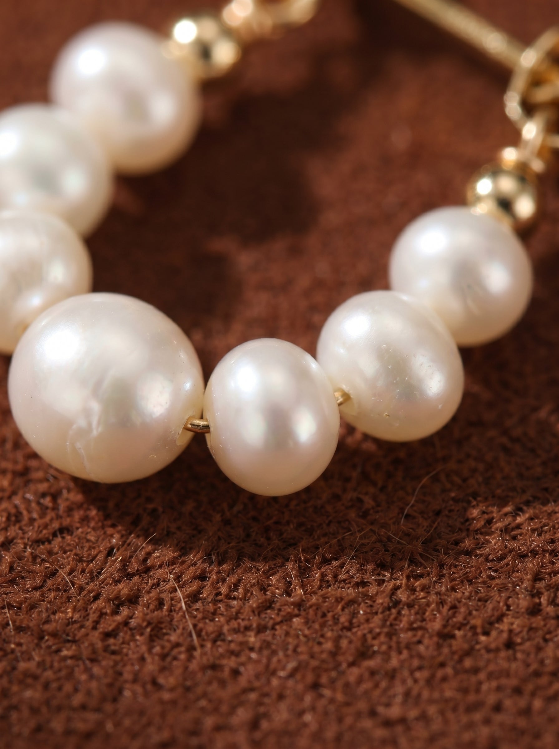 Close-up of Luminous freshwater pearl stud hoop earrings featuring a delicate arrangement of 4mm seed-shaped white pearls and gold accents on a textured brown background.@pearl