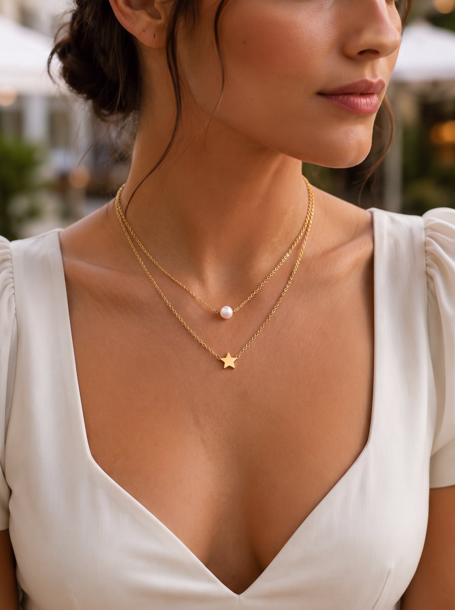 Une femme portant une robe blanche et le collier superposé Luminous Path présentant une breloque étoile dorée et une perle d'eau douce sur de délicates chaînes ton or. @lifestyle