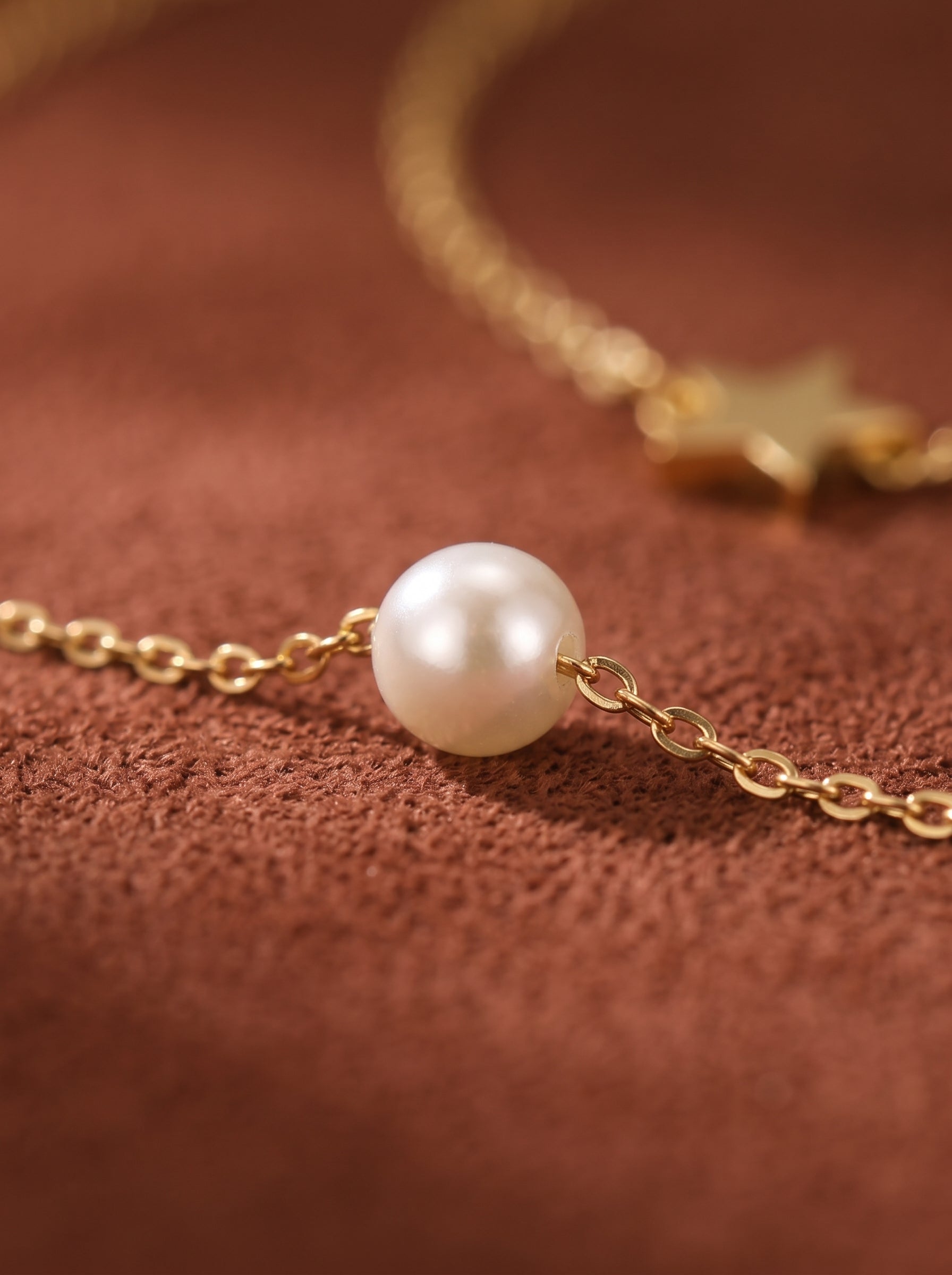Gros plan d'un délicat collier superposé ton or présentant une lustrée perle blanche d'eau douce sur une chaîne et une breloque étoile sur l'autre, présenté sur fond texturé marron. @pearl