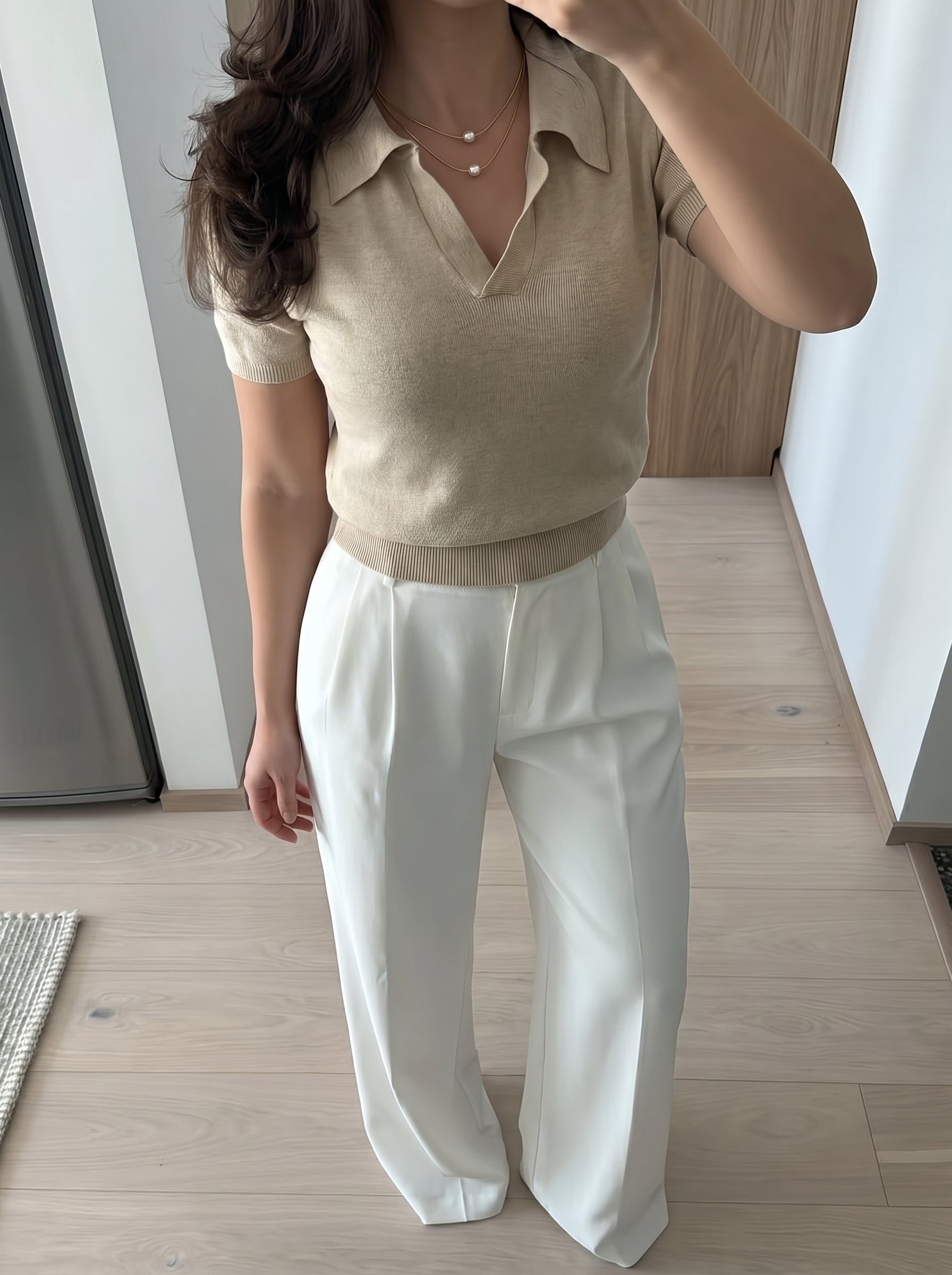 Mannequin portant le collier superposé Lunar Glide présentant deux délicates chaînes serpent ton or avec des perles flottantes d'eau douce, associé à un polo beige et un pantalon blanc évasé. @lifestyle