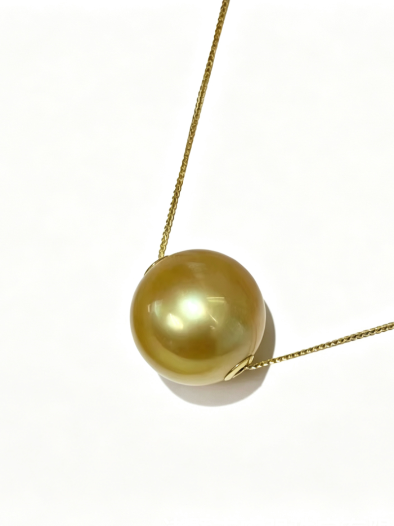 A close-up of a single, lustrous 12mm golden South Sea pearl suspended on a delicate gold chain, appearing to float. The pearl is perfectly round and showcases its natural beauty with a subtle glow against a white background.