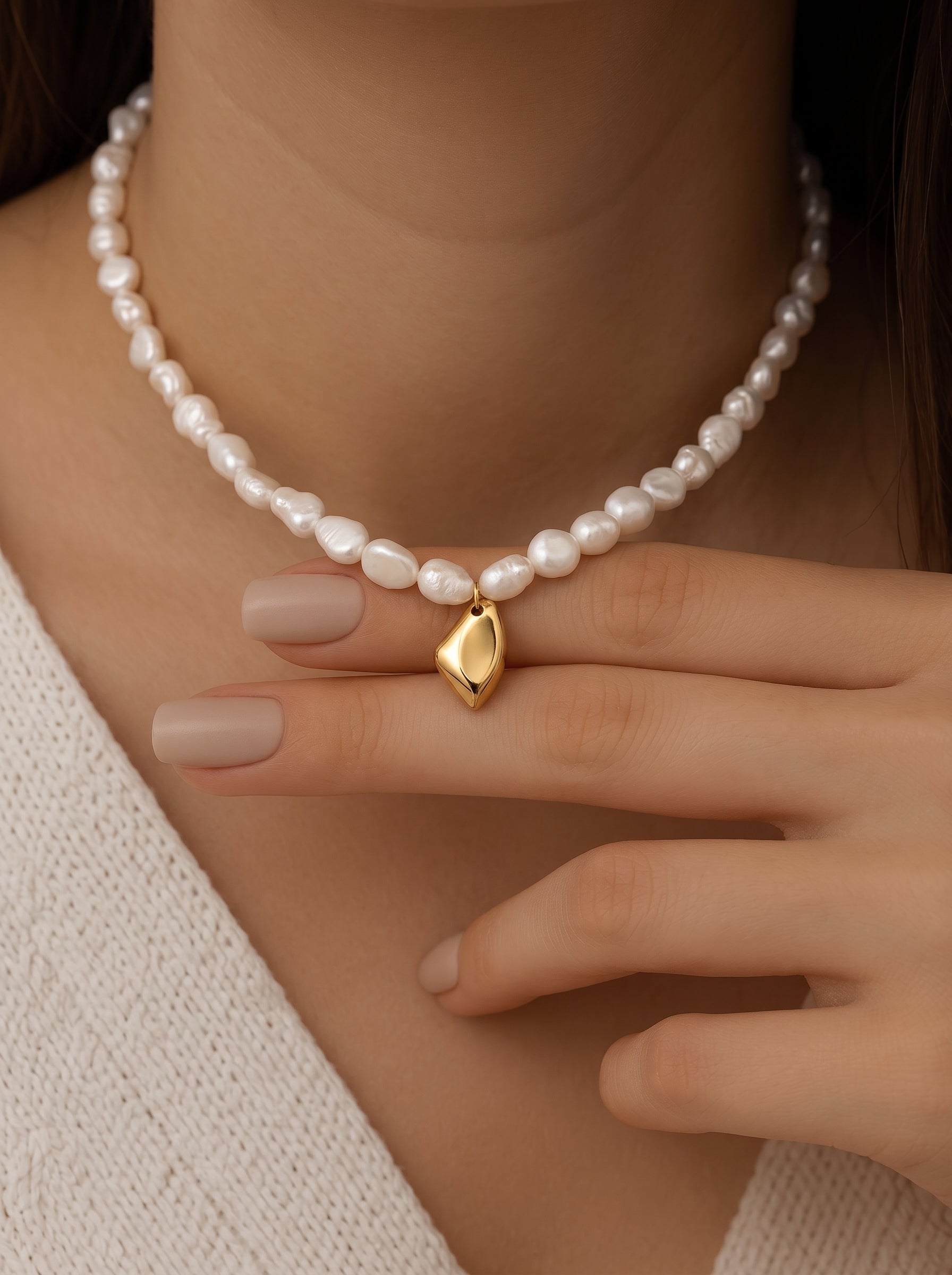 Gros plan du cou d'une femme mettant en valeur le collier perlé pendentif goutte Lyrical en perle d'eau douce, présentant des perles blanches irrégulières et un pendentif organique lisse doré. @model