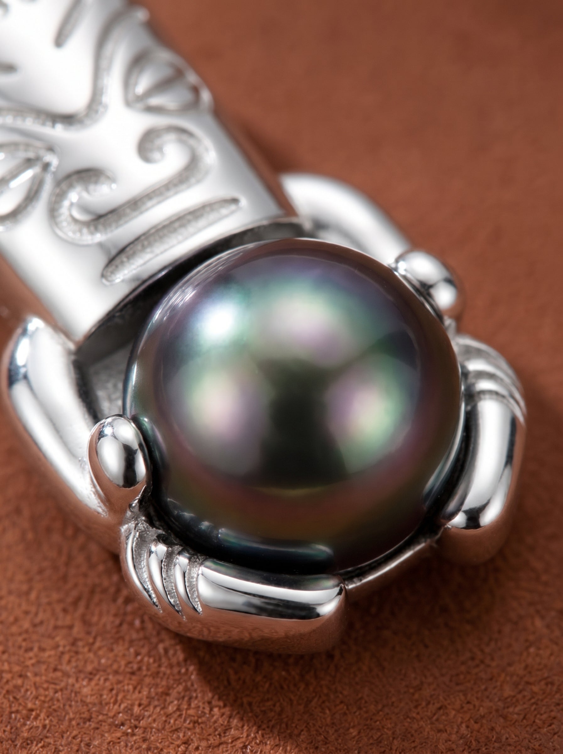 Close-up of a silver Tiki pendant necklace holding a lustrous, dark 10mm Tahitian pearl, showcasing intricate details and iridescent sheen. @pearl