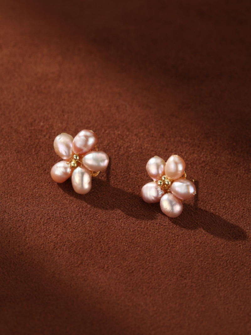 Délicates boucles d'oreilles en grappe florale rose en perle d'eau douce avec des centres en perle dorée, sur fond texturé marron.