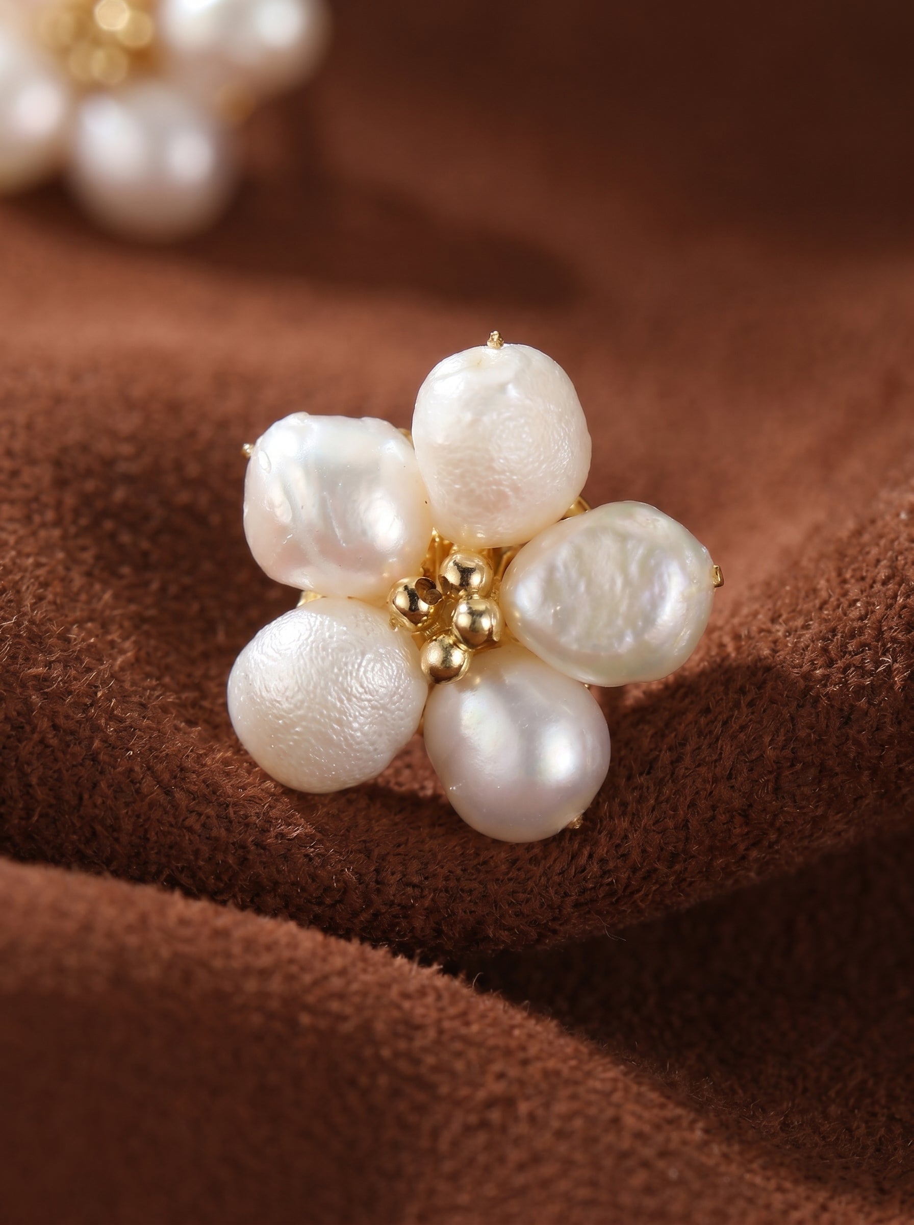 Close-up of Meadow white freshwater baroque pearl flower cluster earrings with gold bead details on a brown textured background @pearl