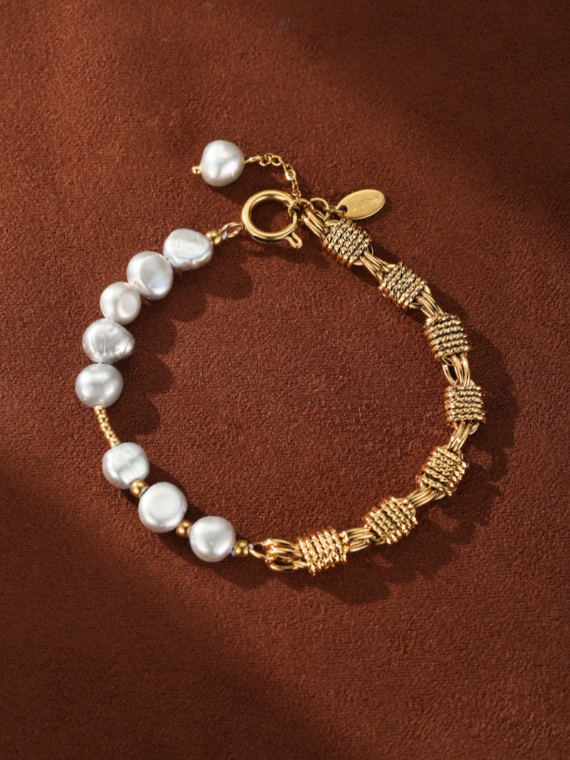 Gold-toned bracelet featuring a mesh weave chain on one side and a strand of luminous white freshwater pearls on the other, set against a brown textured background.