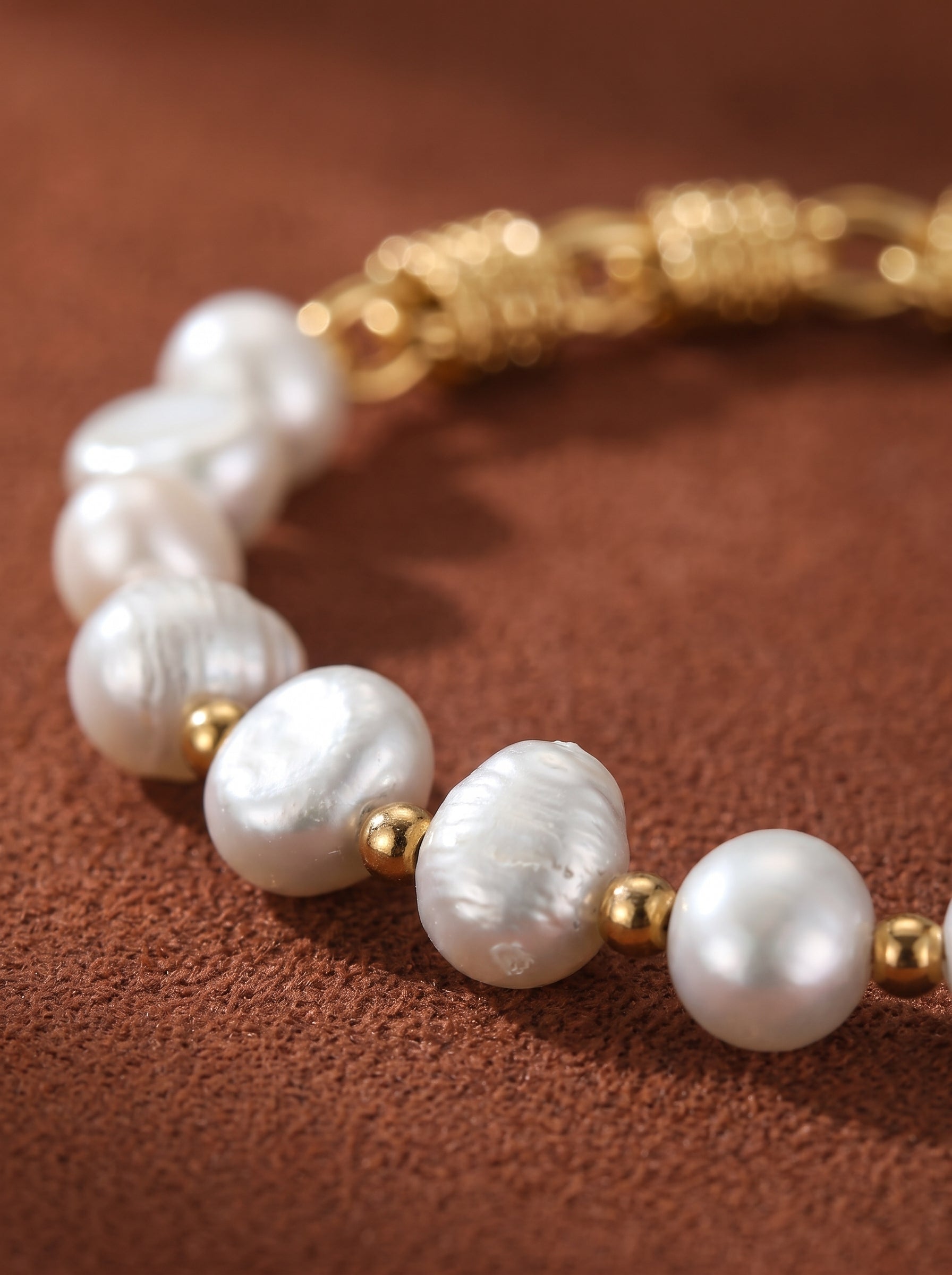 Close-up of a Mesh Weave bracelet featuring irregular white freshwater pearls interspersed with small gold beads, with a textured gold chain visible in the background.