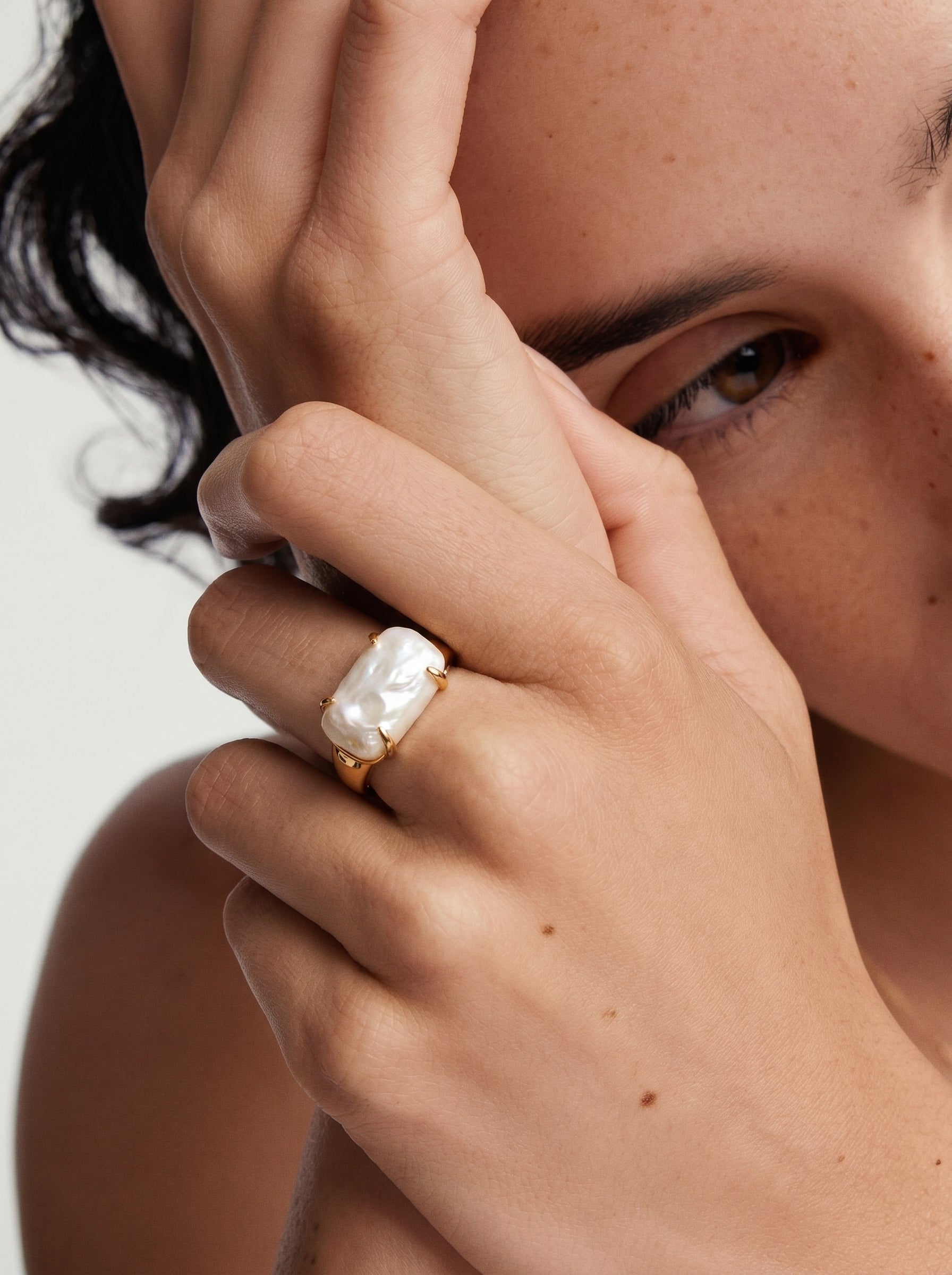 A close-up shot of a hand wearing the Monolith Freshwater Pearl Cuff Ring, featuring a large, irregular white baroque pearl set in a gold cuff band. @model