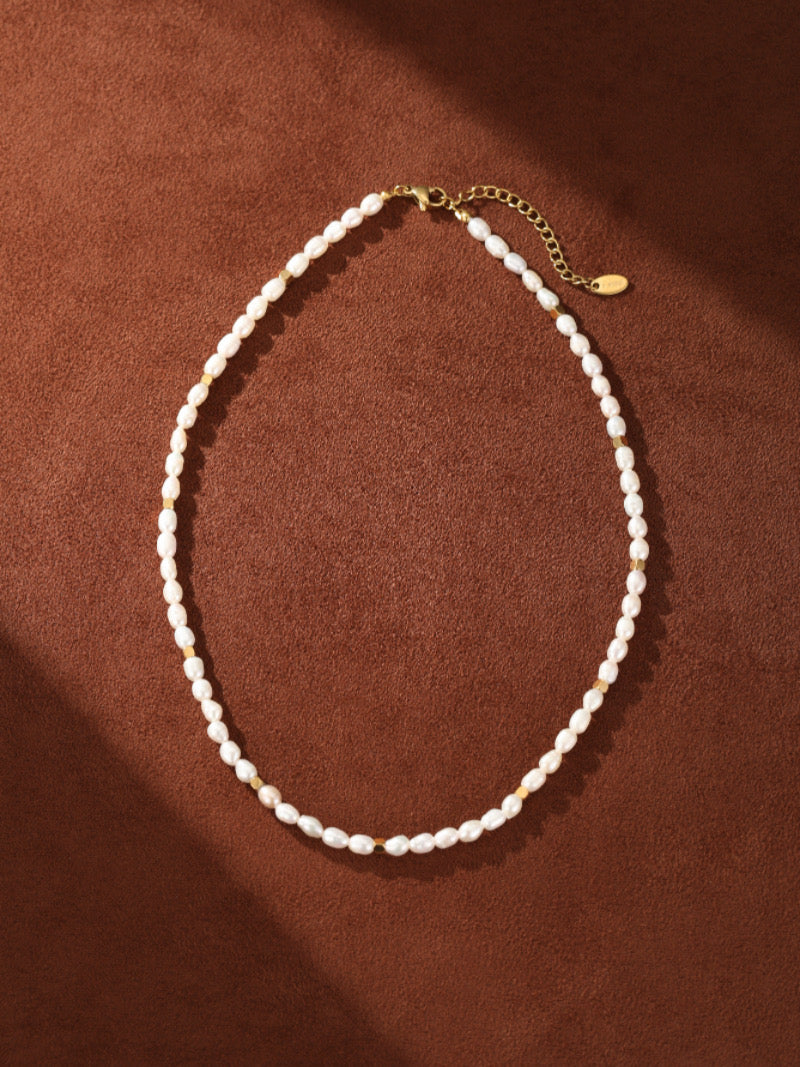 Collier pendentif perlé pièce Mythos en perle d'eau douce avec perles graines de 5 mm et fermoir doré sur fond marron.