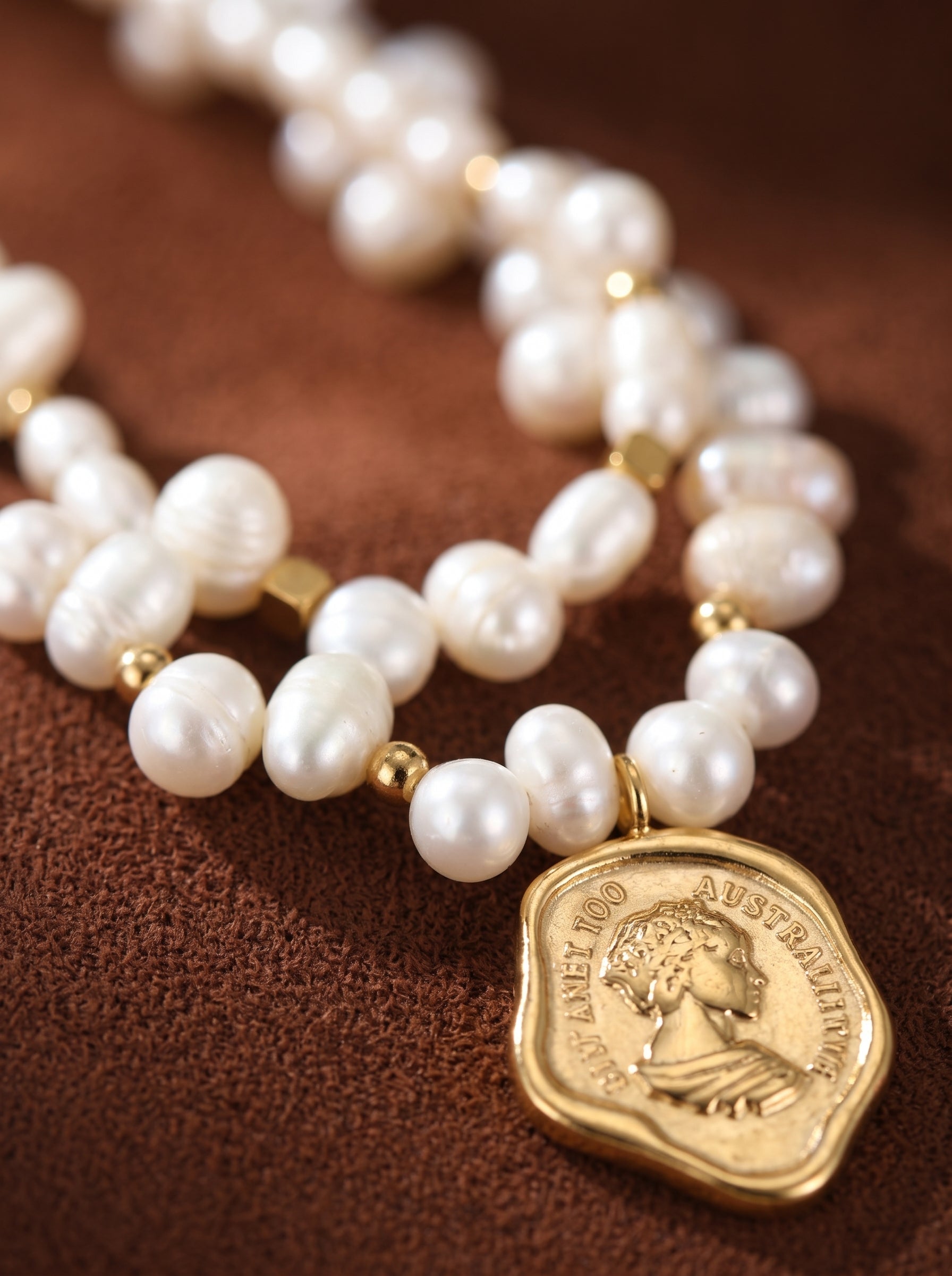 Collier pendentif pièce Mythos présentant un double rang de perles blanches irrégulières d'eau douce et des accents dorés, avec un pendentif pièce doré montrant un profil de la reine Elizabeth II. @pearl