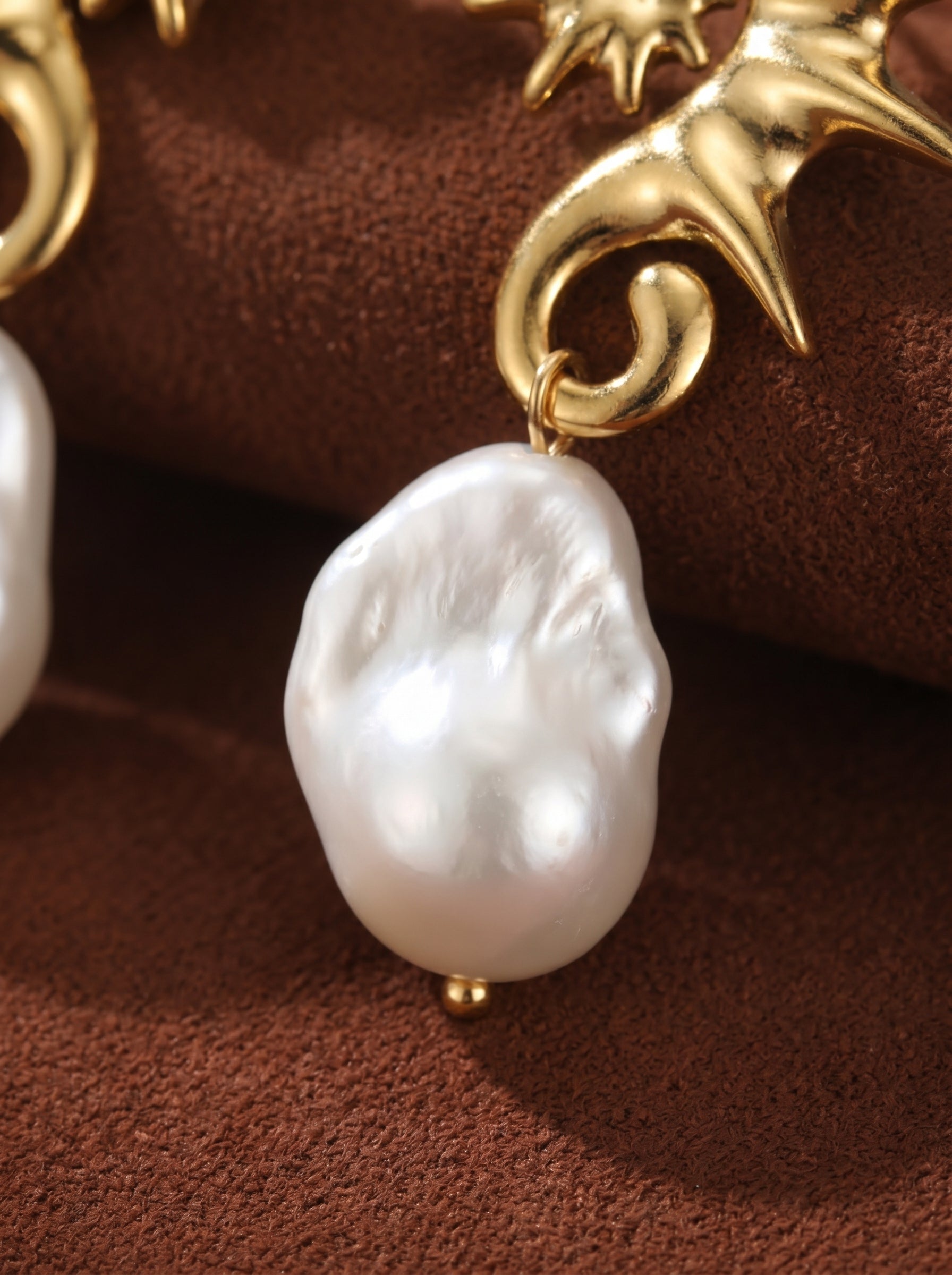 Close-up of a Nautilus freshwater pearl shell dangle stud earring, showcasing a large, irregular white baroque pearl with a gold stud accent against a textured brown background. @pearl