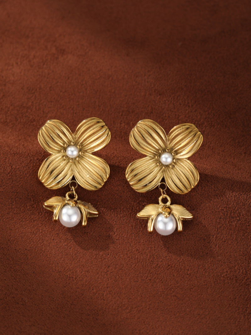 Boucles d'oreilles goutte florales ton or avec une perle centrale et une breloque inspirée d'une abeille tenant une plus grande perle en dessous.