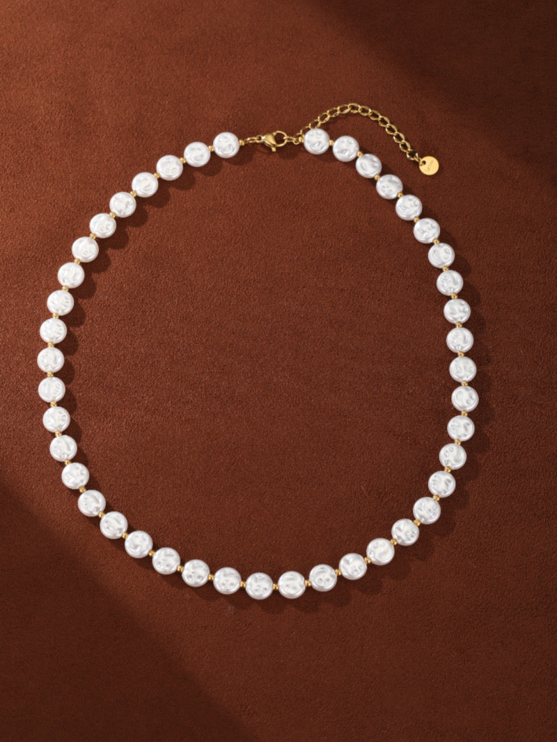 A delicate gold-toned chain necklace with alternating white baroque freshwater pearls and gold beads. The necklace is laid out in a curve on a brown background.