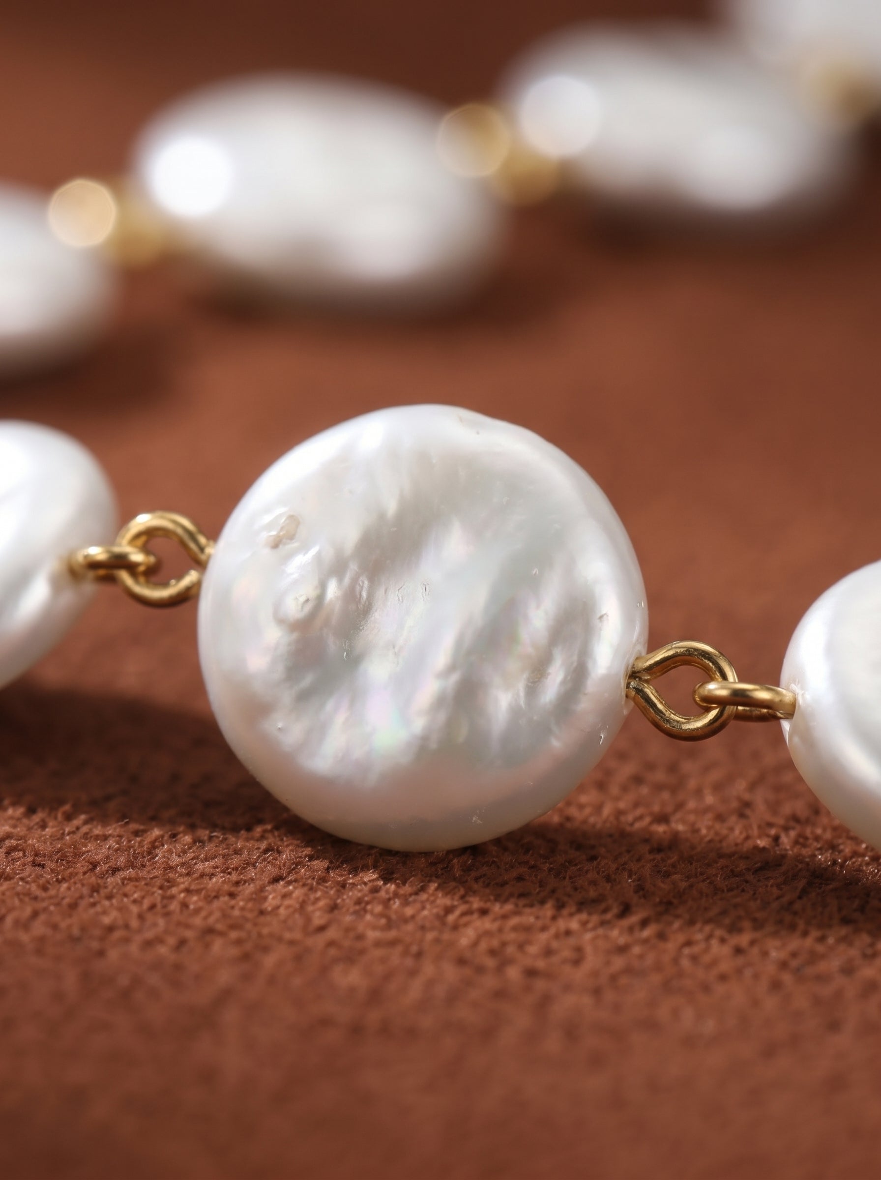 Close-up of the Odyssey necklace featuring large, lustrous white baroque imitation pearls with a hammered texture, connected by gold-tone links on a brown textured background. @pearl