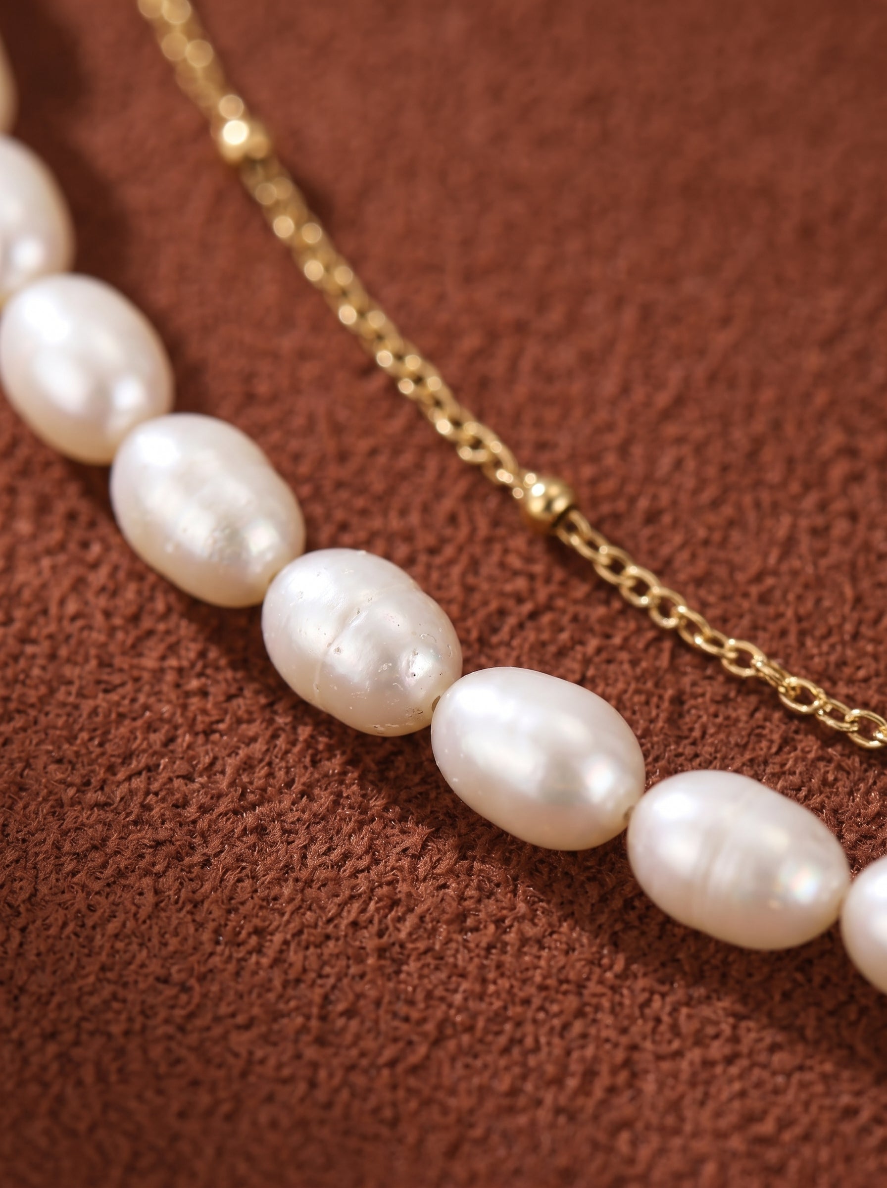 Gros plan d'un collier superposé présentant un rang de perles blanches irrégulières d'eau douce aux côtés d'une délicate chaîne ton or. @pearl