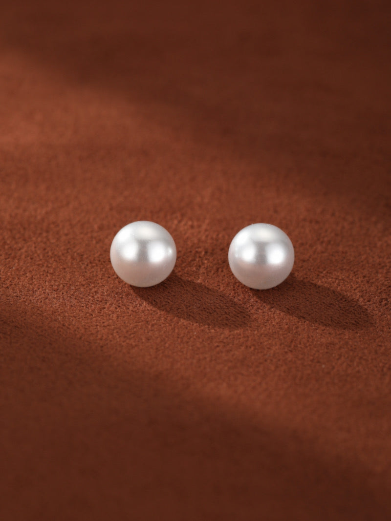 Deux lustrées perles blanches d'eau douce de formes variées reposent sur une surface texturée marron, projetant de douces ombres.
