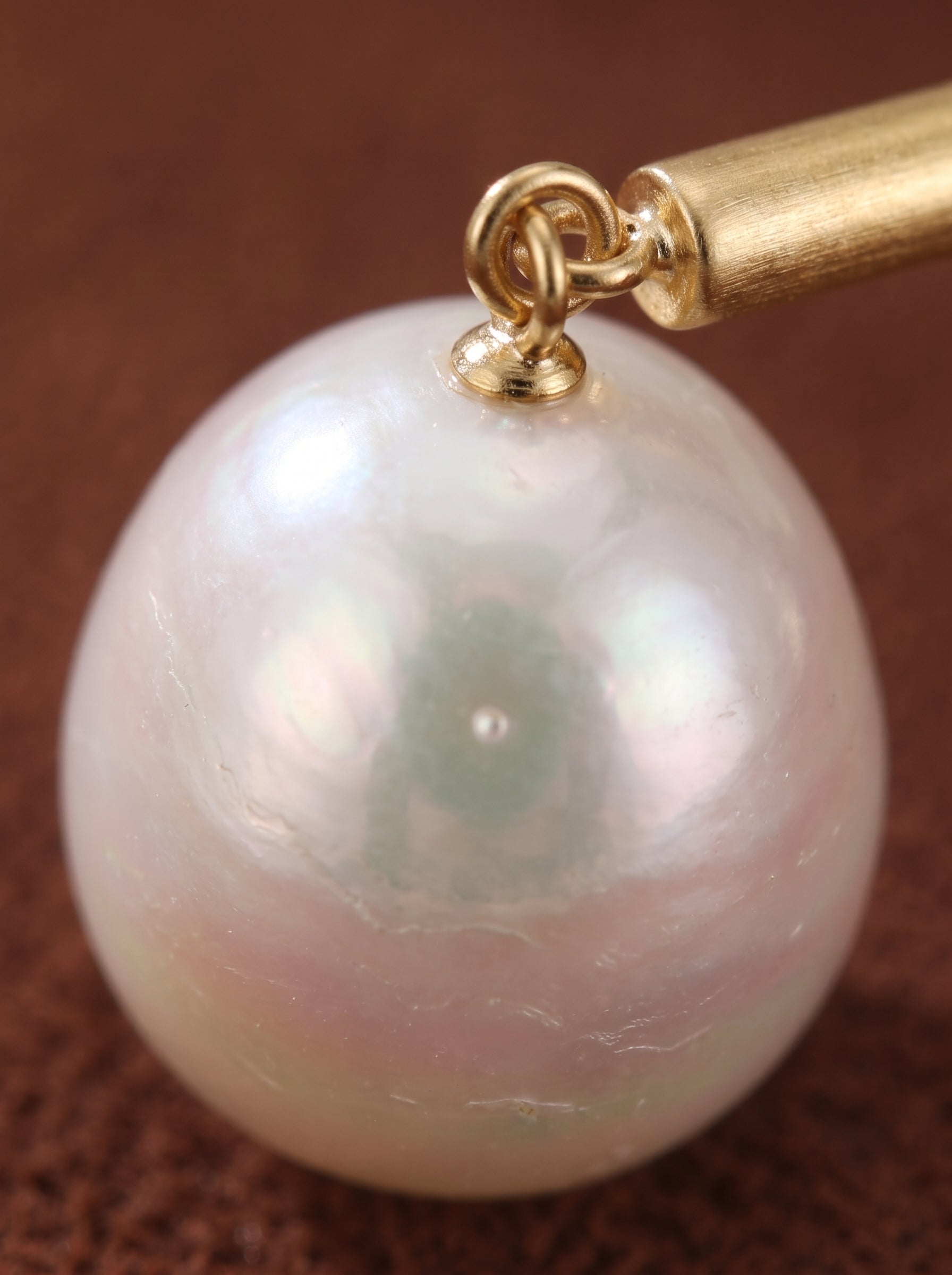 Gros plan d'une seule et lustrée boucle d'oreille en perle blanche d'eau douce avec un accent barre ton or, mettant en valeur son éclat naturel et sa subtile irisation. @pearl