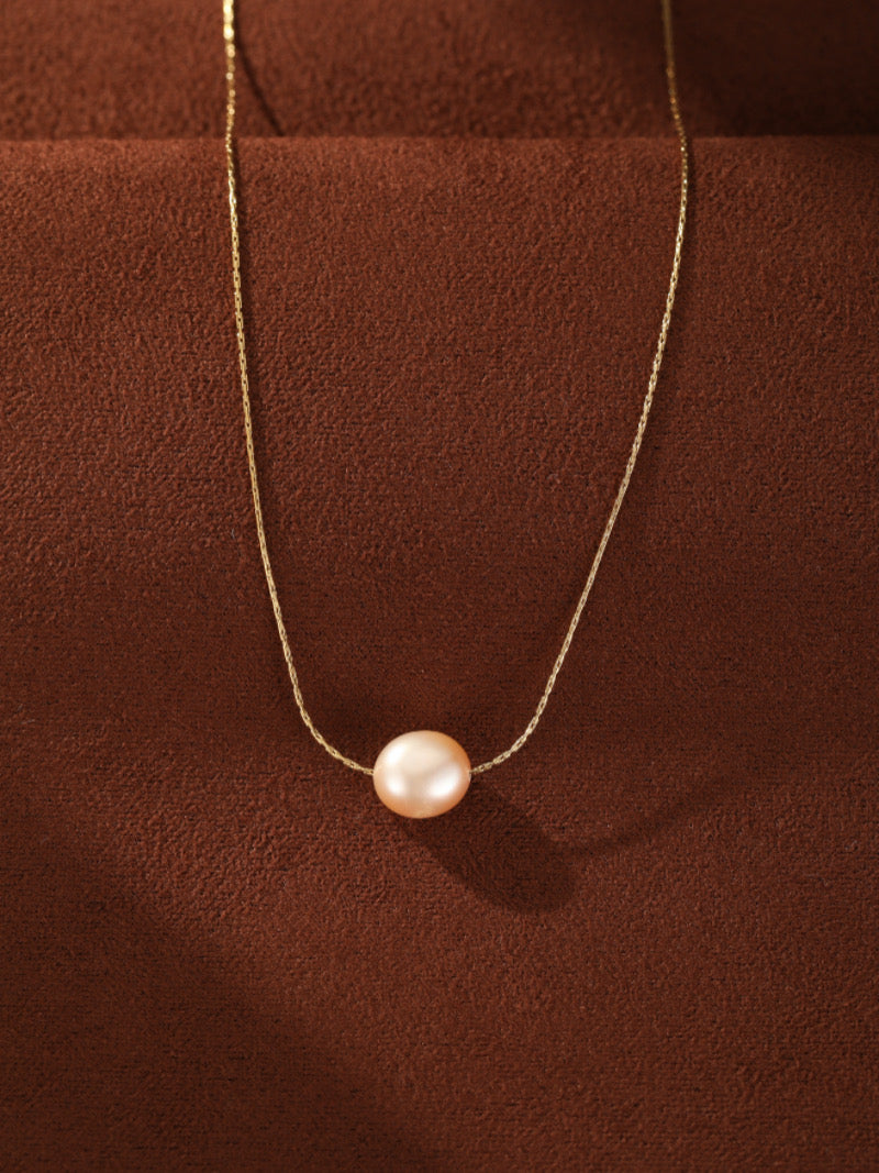 Un délicat collier à chaîne dorée avec une seule et lustrée perle rose pendante d'eau douce au centre, sur fond texturé marron.