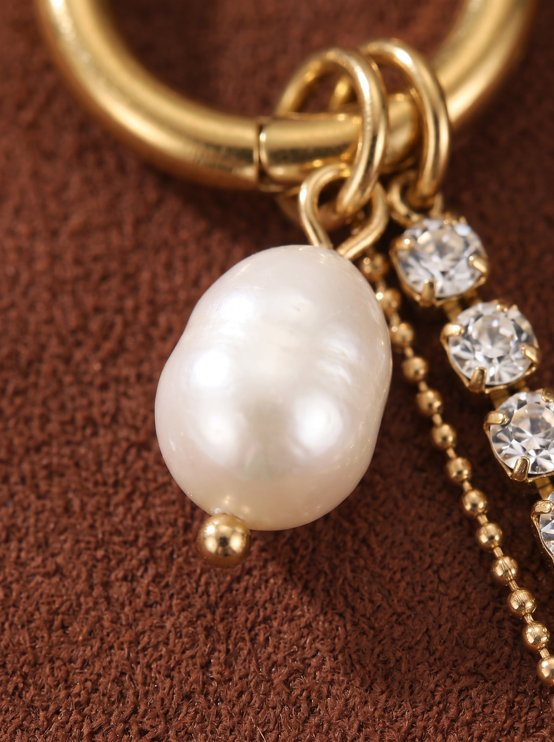 Close-up of a gold hoop earring with a dangling baroque freshwater pearl, a delicate gold chain, and sparkling crystals. @pearl