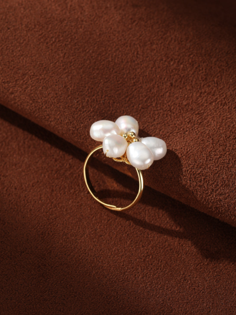 A gold cuff ring featuring a delicate flower design with five irregular white freshwater baroque pearls on a textured brown background.