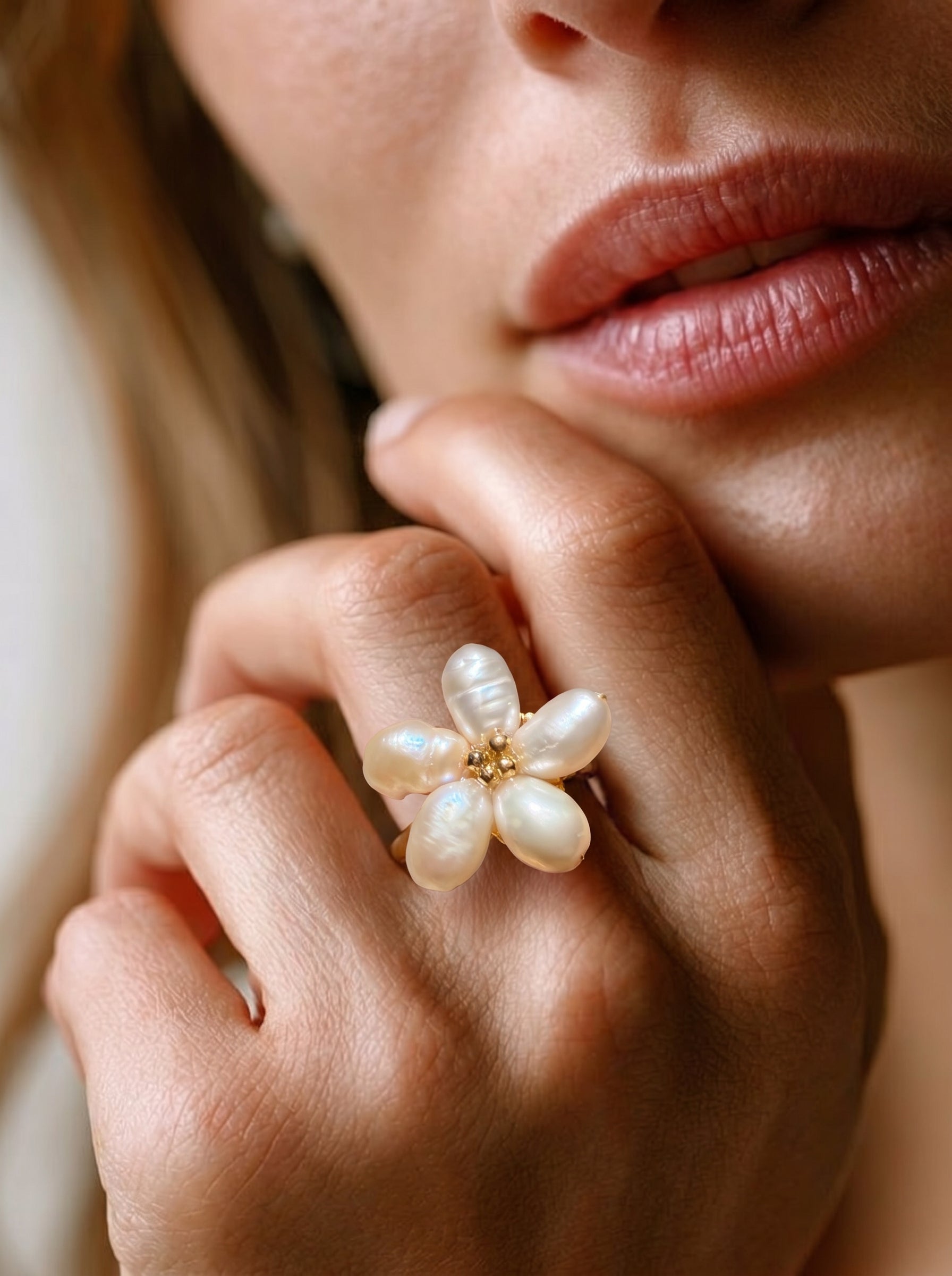 Close-up of a hand wearing a Radiance freshwater pearl flower cuff ring, featuring five irregular white baroque pearls arranged like a bloom with a gold beaded center. #model