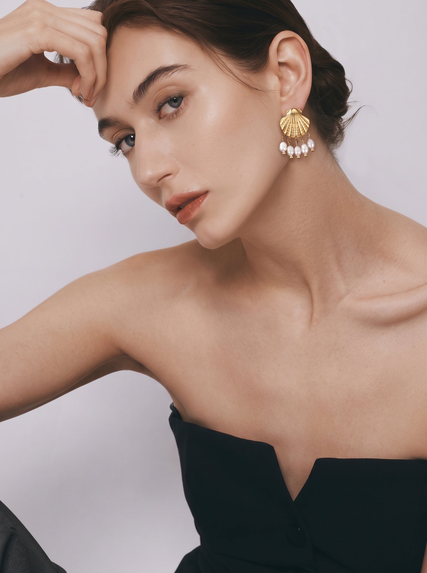Une femme portant des boucles d'oreilles pendantes coquillage dorées avec cinq perles blanches d'eau douce pendant de chaque boucle d'oreille. @model