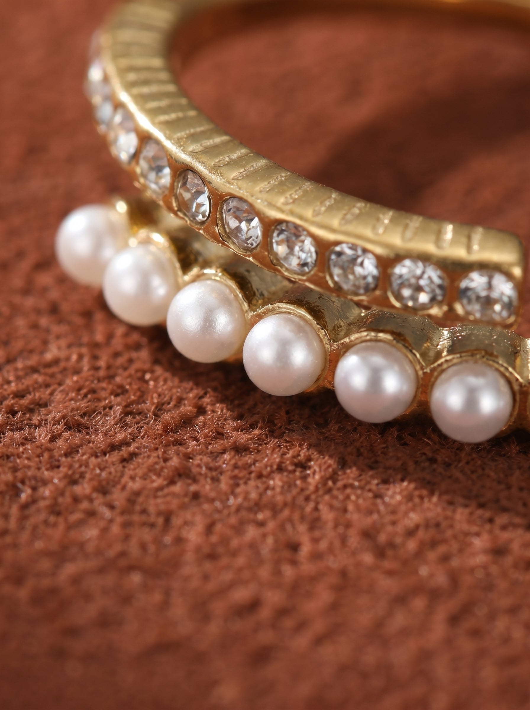 Close-up of a gold-toned cuff ring featuring a dual-band design, one band adorned with clear crystals and the other with small white imitation pearls. @pearl