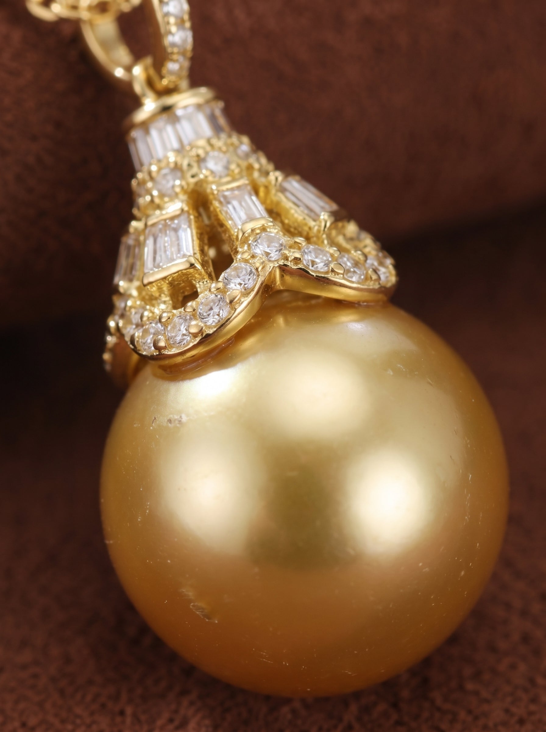 Close-up of a large, lustrous golden South Sea pearl pendant necklace with a diamond-encrusted cap featuring round and baguette-cut diamonds. @pearl