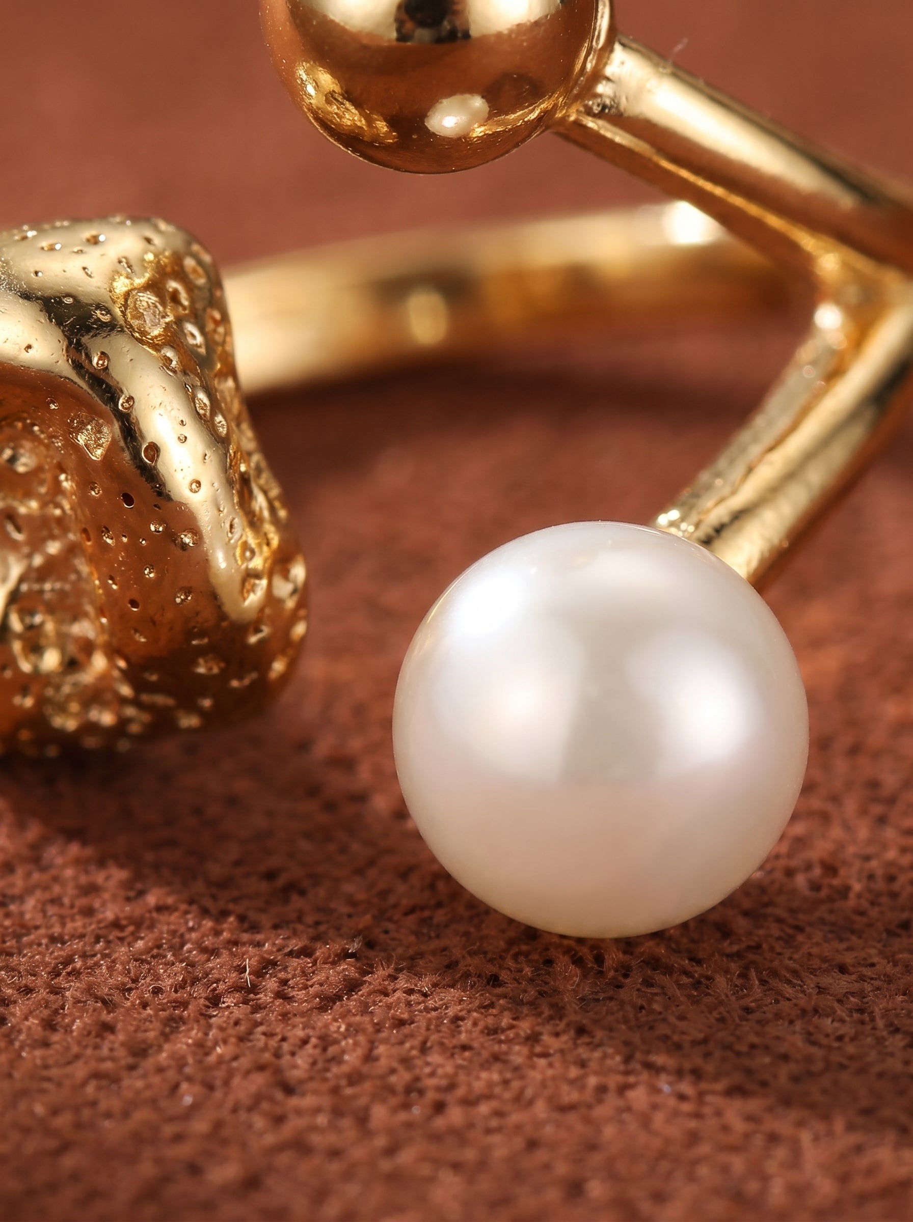 Close-up of a gold-toned open ring featuring a textured nugget detail and a smooth white freshwater pearl.@pearl