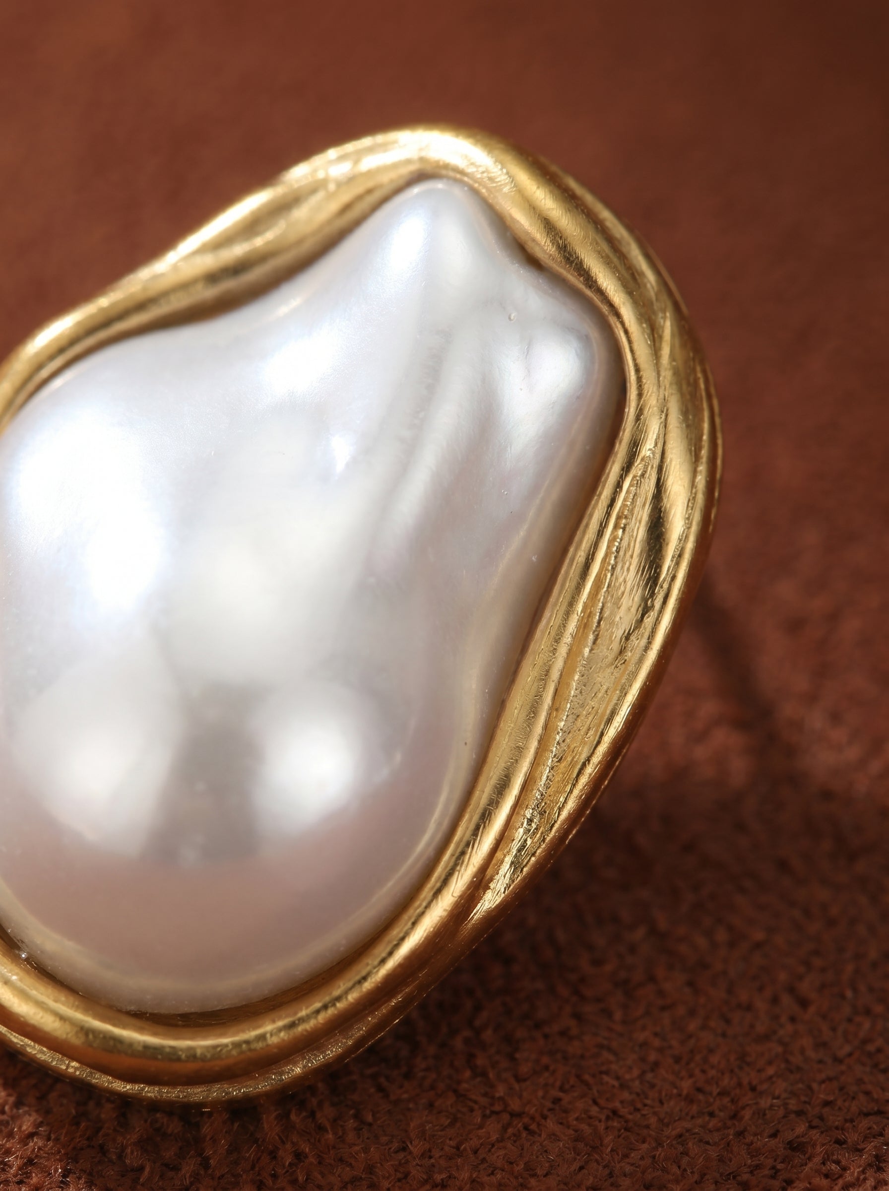 Close-up of a single Sculpted earring featuring a large, lustrous white freshwater baroque pearl encased in a textured golden-toned frame. The pearl has an organic, irregular shape, highlighting its natural beauty.@pearl