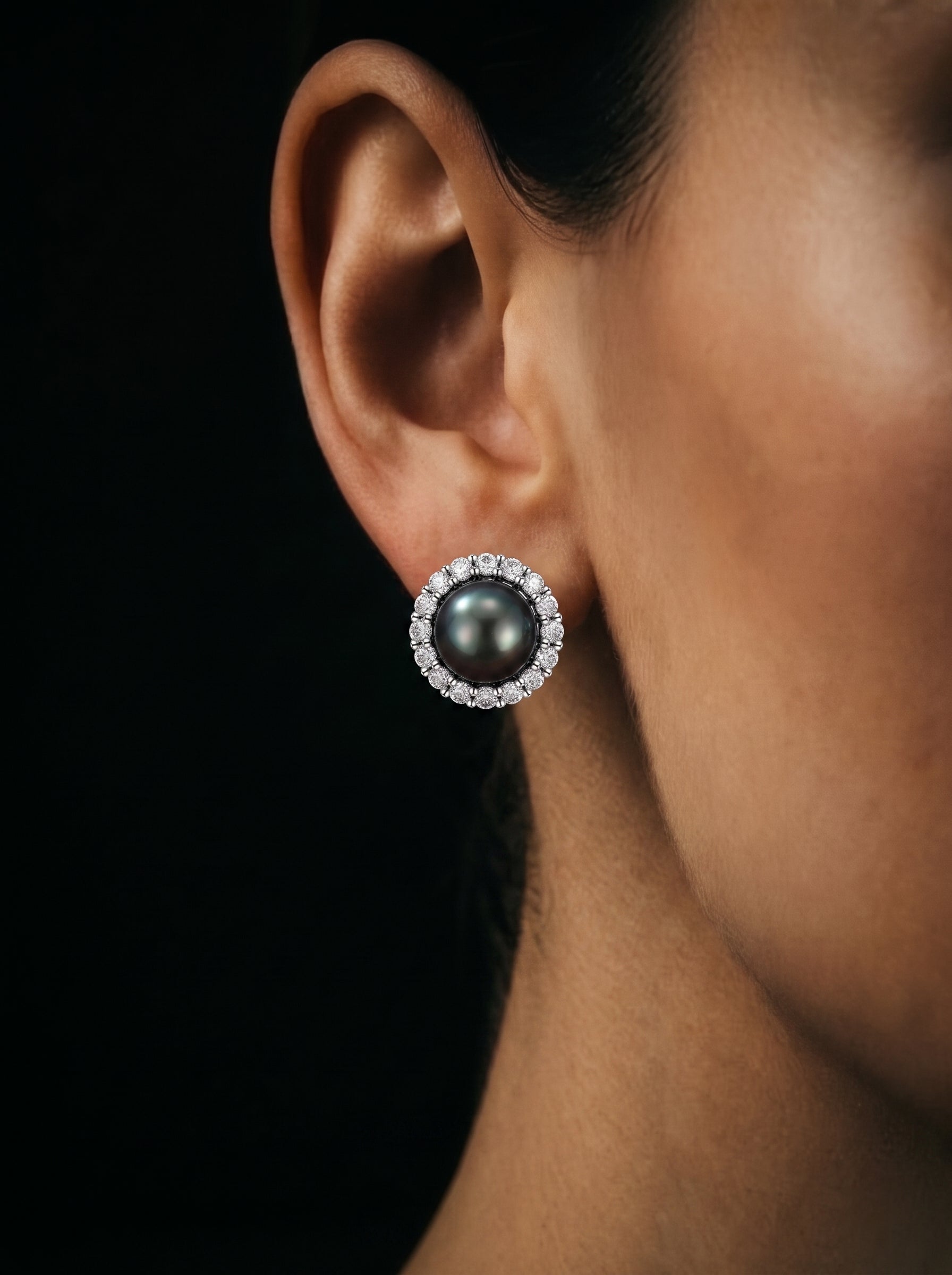 Close-up of a model's ear showcasing a Shadowlight Tahitian Pearl halo stud earring surrounded by sparkling diamonds. @model