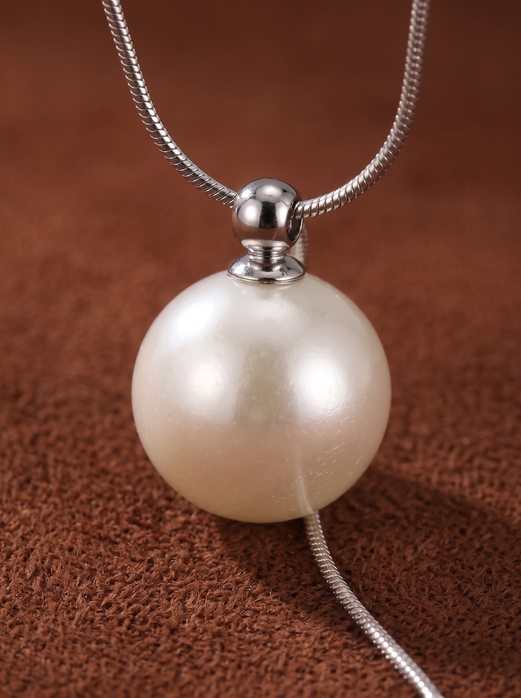 Sheen - Freshwater Pearl Long Necklace featuring a single, luminous 8mm round white freshwater pearl suspended from a delicate silver chain. The pearl has a smooth surface and a subtle glow, showcased against a textured brown background. @pearl
