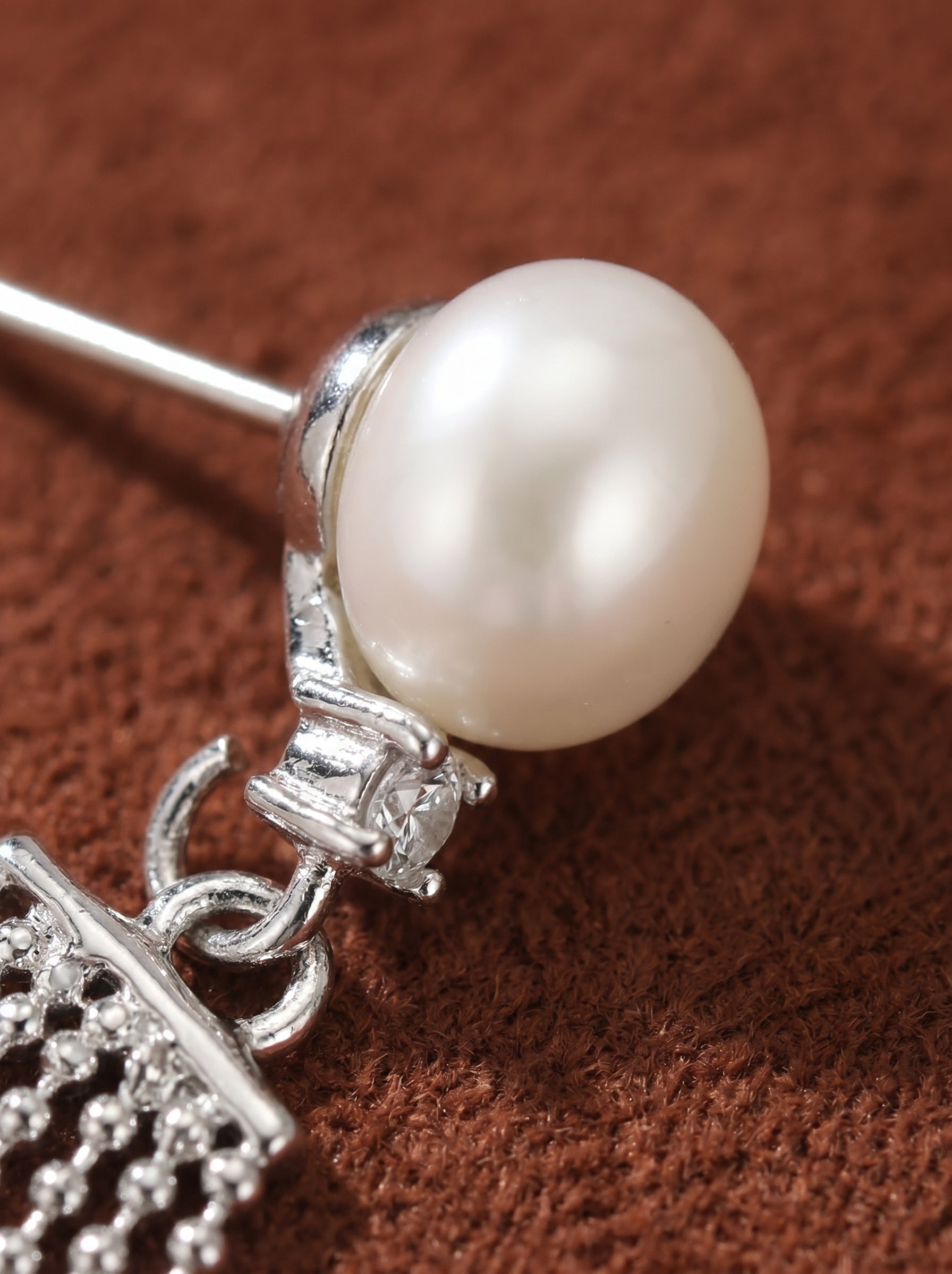 Close-up of a single Shimmer Freshwater Pearl Dangle Stud Earring featuring a lustrous white button pearl, a sparkling accent stone, and delicate silver chains against a textured brown background. @pearl
