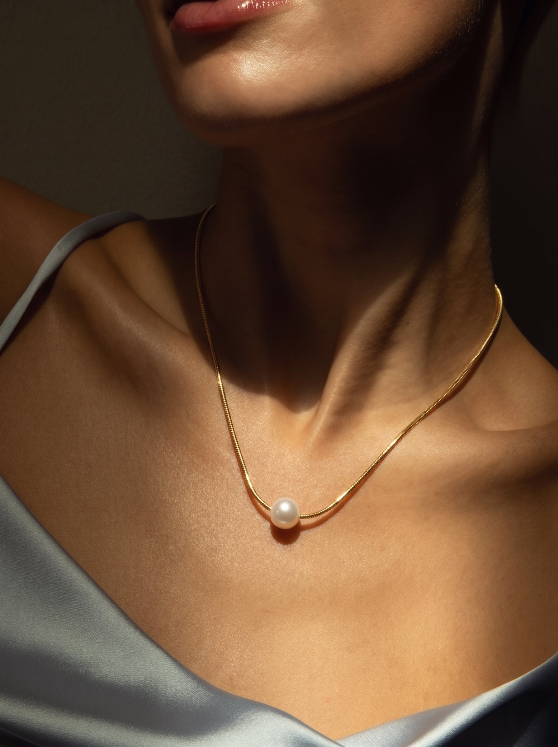 Close-up of a woman wearing the Solace Small Pendant Necklace, featuring a single 6 mm white freshwater seed pearl on a delicate gold-toned chain.@model