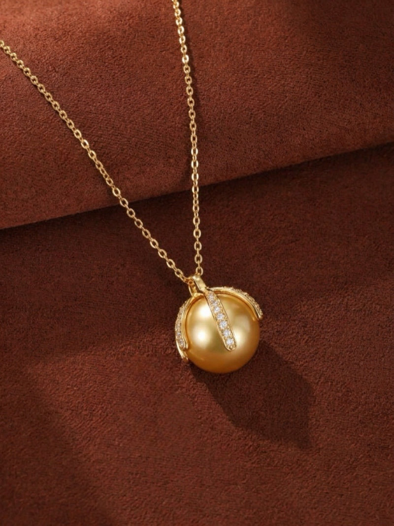 Solara 12mm Golden South Sea Pearl pendant necklace with sparkling gemstone accents on a gold chain, set against a brown textured background.