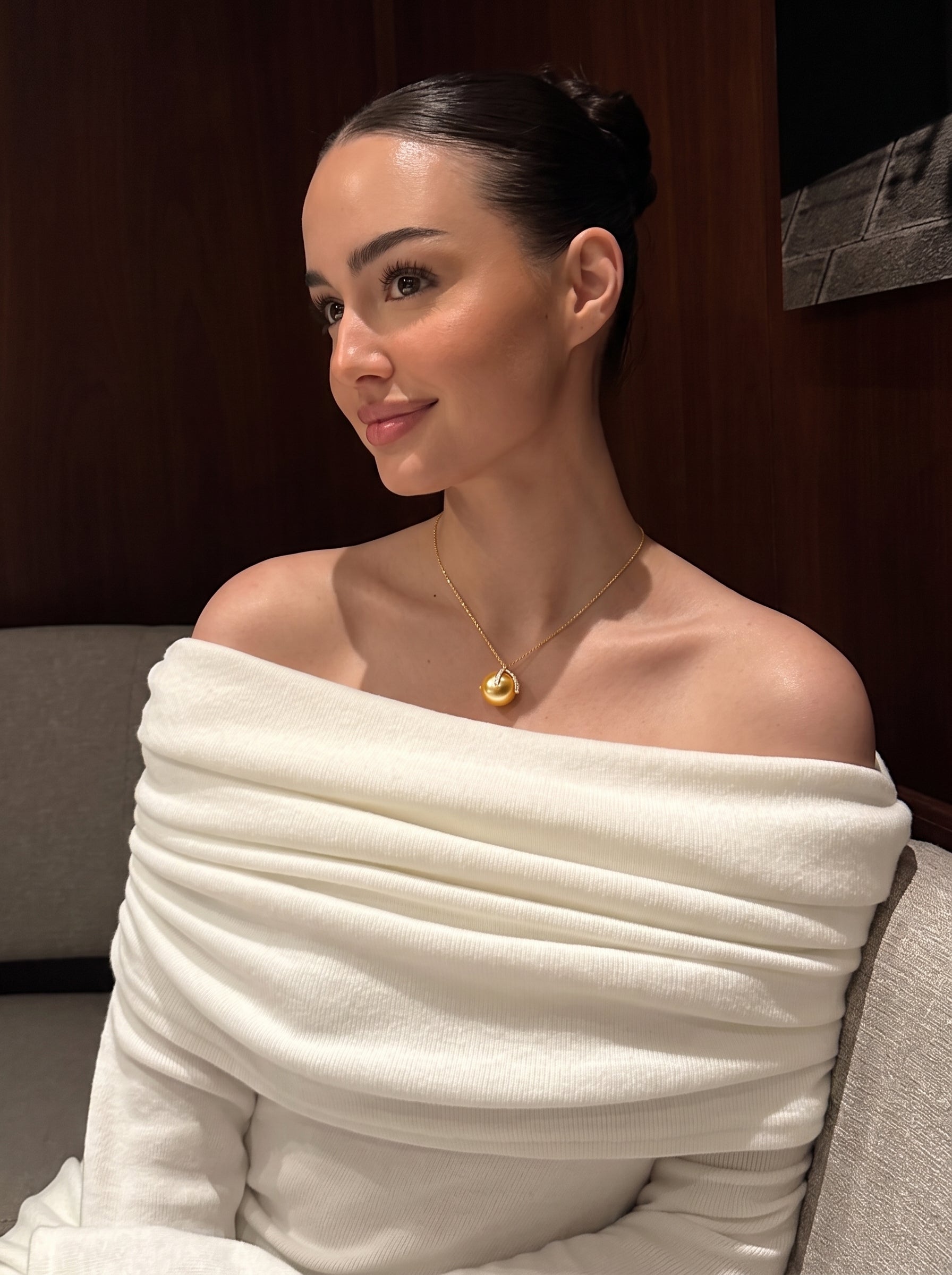 A woman wearing the Solara South Sea Pearl Pendant Necklace featuring a lustrous 12mm golden pearl in a polished gold-tone setting with gemstone accents, styled with a white off-the-shoulder top. @lifestyle
