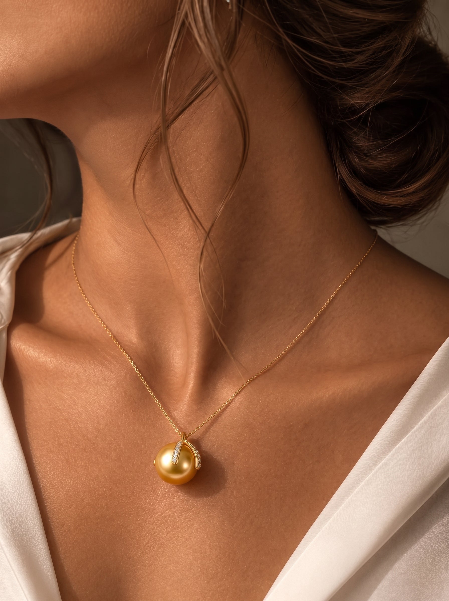 Une femme porte le collier pendentif Solara en perle des mers du Sud, présentant une grande et lustrée perle dorée des mers du Sud de 12 mm dans une monture moderne ton or avec des accents diamant sur une délicate chaîne dorée. @model