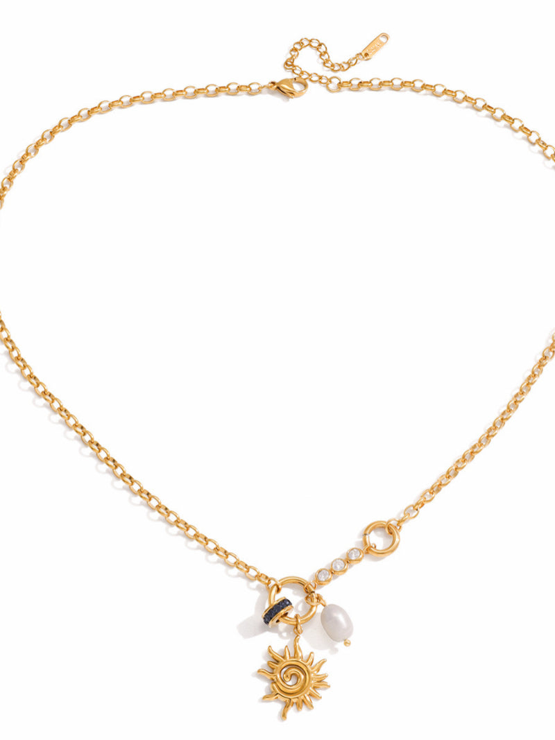 Gold-tone chain necklace featuring a sun pendant, a freshwater pearl, and sparkling stones, with a small blue accent. @pearl