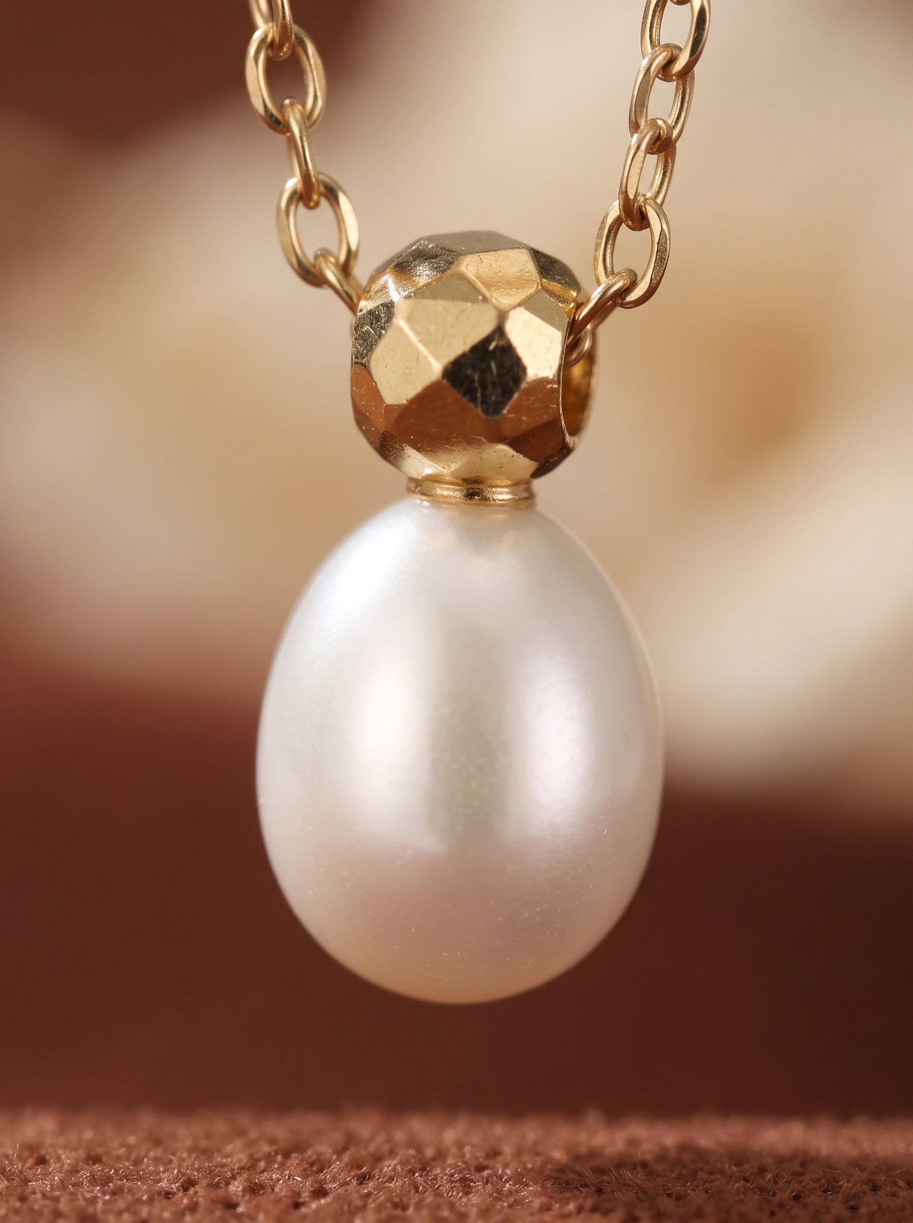 Gros plan d'un collier pendentif goutte en perle graine blanche d'eau douce avec une perle dorée facettée et une délicate chaîne dorée. @pearl