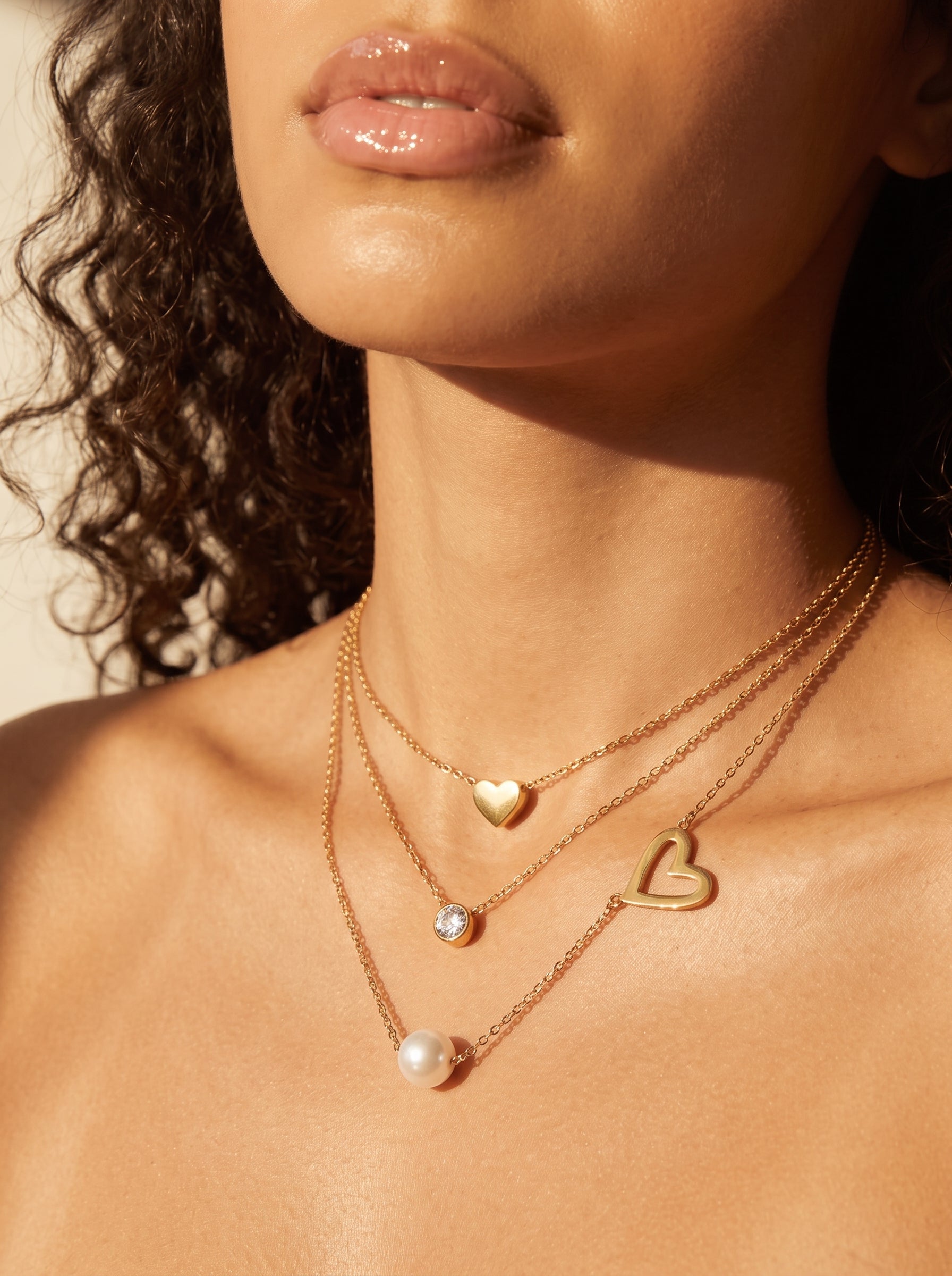 Collier superposé Soulful présentant une perle blanche d'eau douce, un cristal scintillant, et deux breloques cœur dorées sur une mannequin. @model