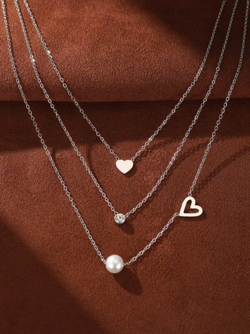 Collier superposé Soulful avec une petite breloque cœur, une pierre accent scintillante, et une lumineuse perle blanche d'eau douce sur la chaîne inférieure, avec une breloque cœur ajourée sur le côté. Métal ton argent.